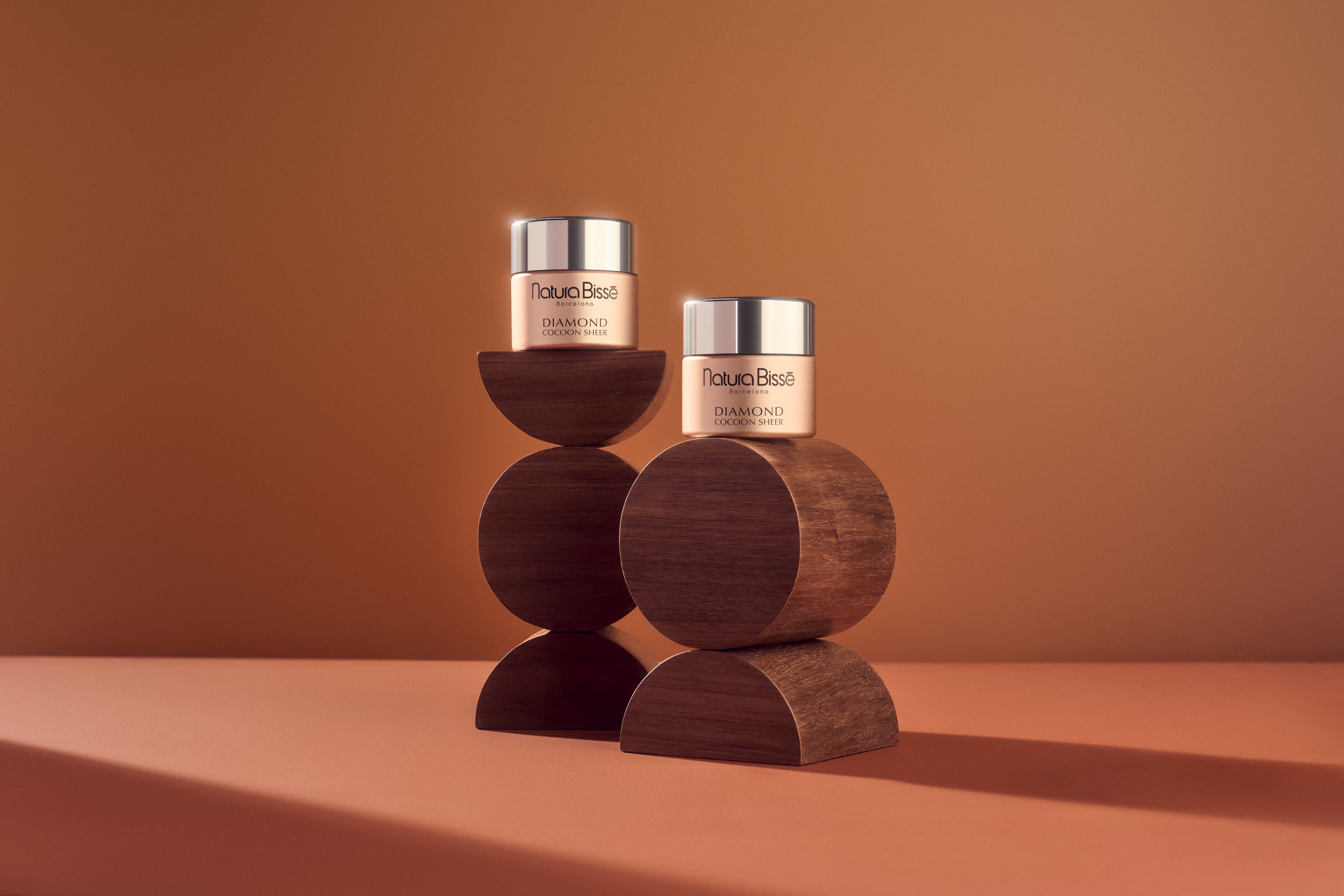 Natura Bissé Stabilizing skincare collection displayed on textured stone pedestals in a warm neutral setting, featuring a cleanser, purifying concentrate, resurfacing essence, cleansing mask, and oil-free gel cream.