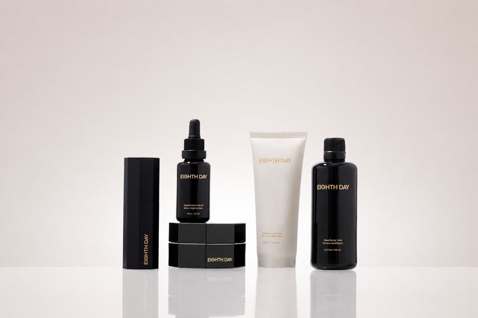 Eighth Day skincare collection featuring a treatment stick, regenerative serum, restorative cleanser, moisturizer, and resurfacing tonic displayed on a reflective surface against a soft cream background.