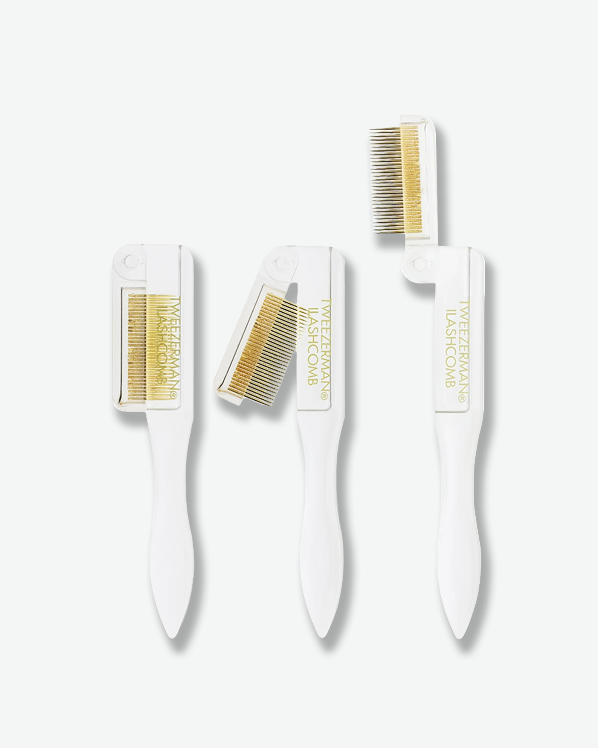 Product shot demonstrating three stages of opening a folding Tweezerman Ilashcomb against a plain gray background. The white plastic tool is shown completely folded on the left, half-unfolded in the middle, and fully extended on the right, revealing fine gold-colored metal comb teeth.