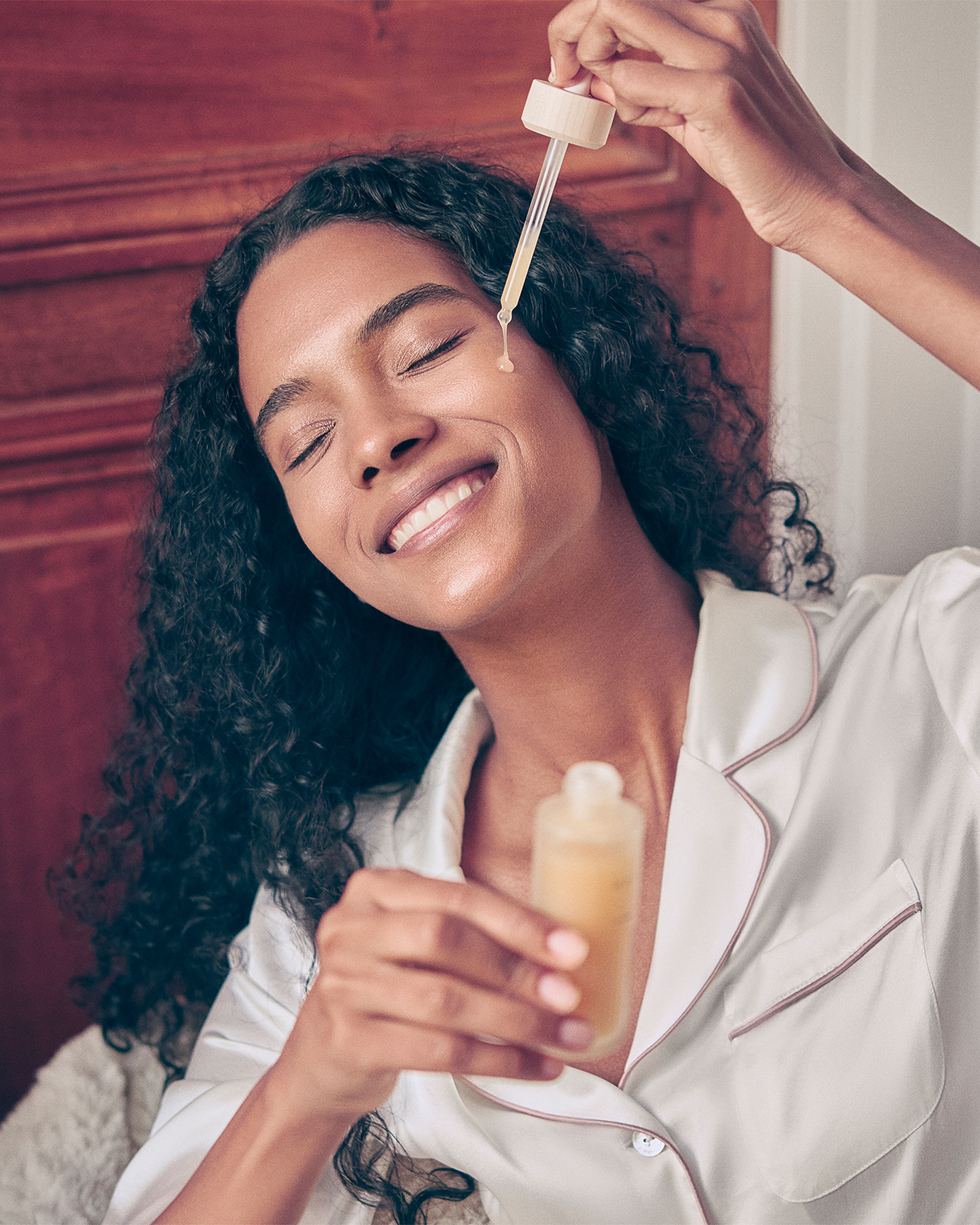 Woman applying a dropper of liquid to her face, smiling.