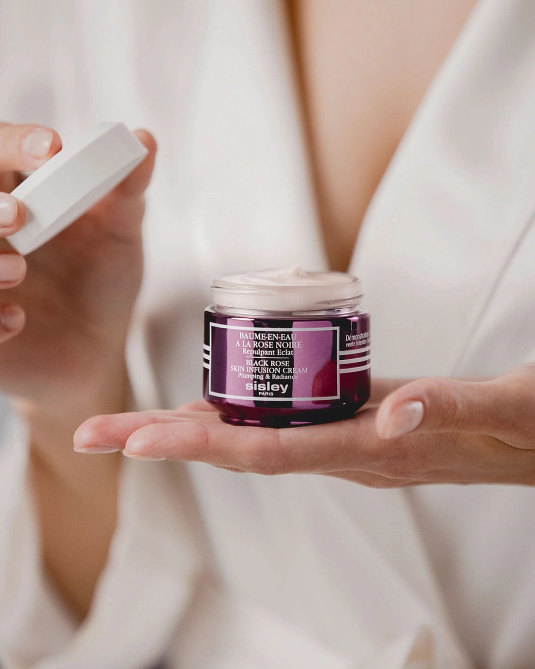 Person holding a jar of skincare product with a blurred background