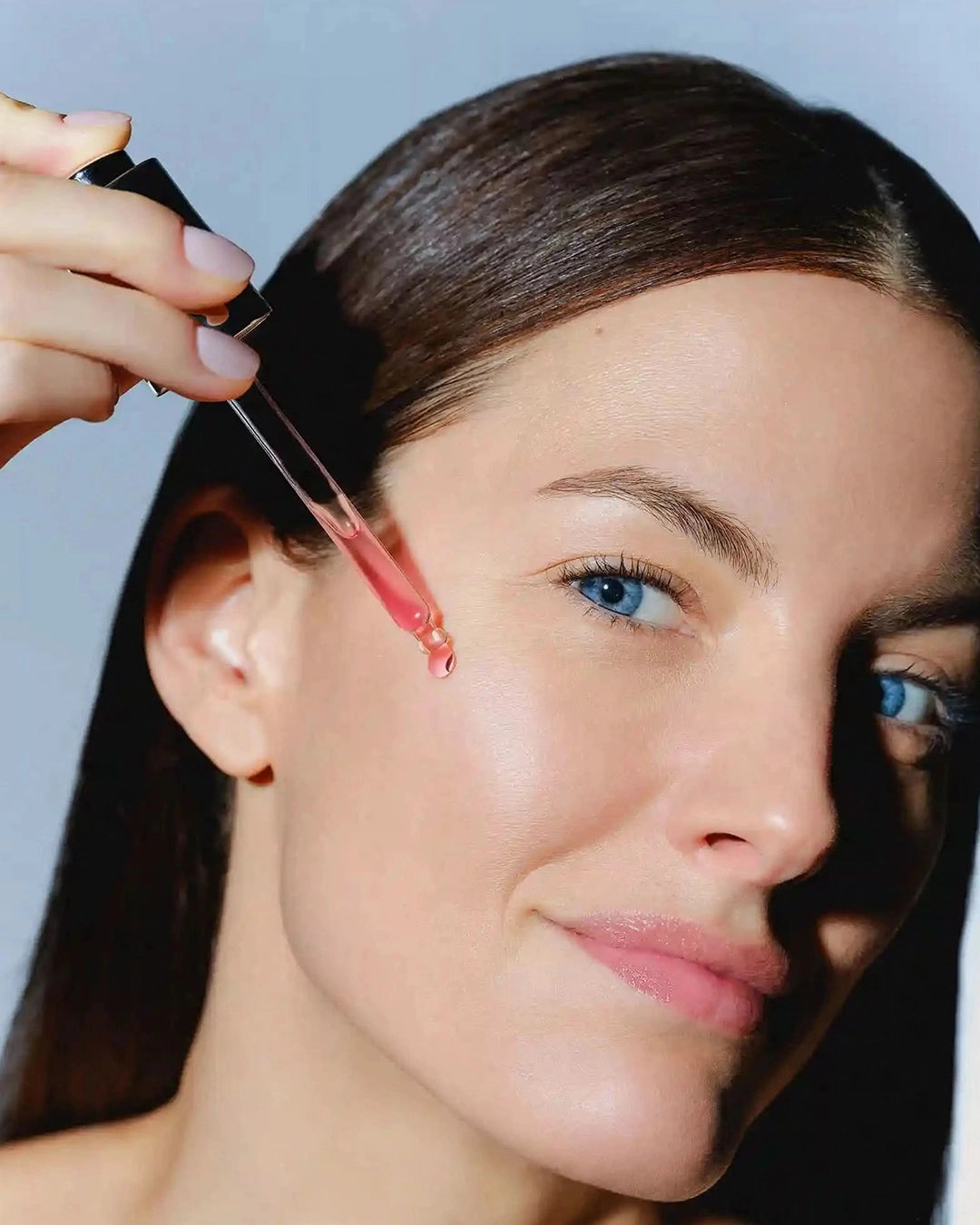 Woman applying a cosmetic product to her face with a serum dropper