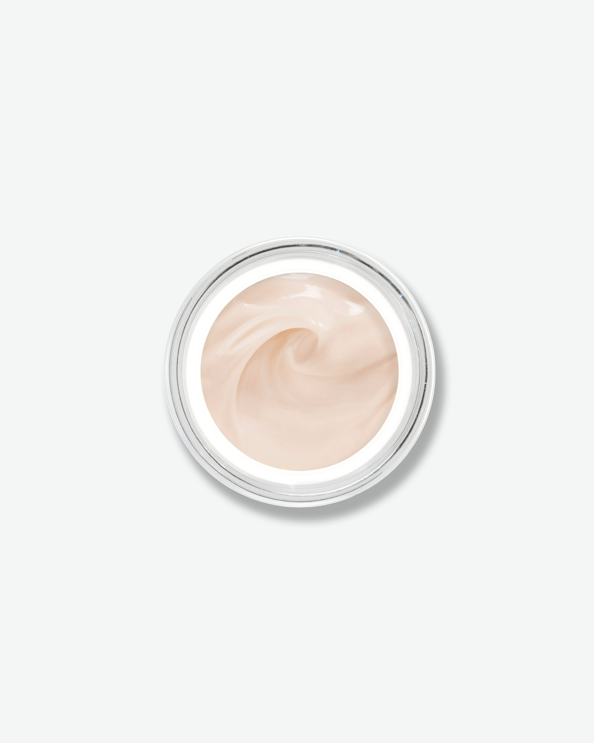 Overhead, top-down view looking directly into an open skincare jar against a plain gray background. The smooth, light-colored glass rim encircles a soft, pale peach-tinted face cream that is textured with an elegant swirl in the center.