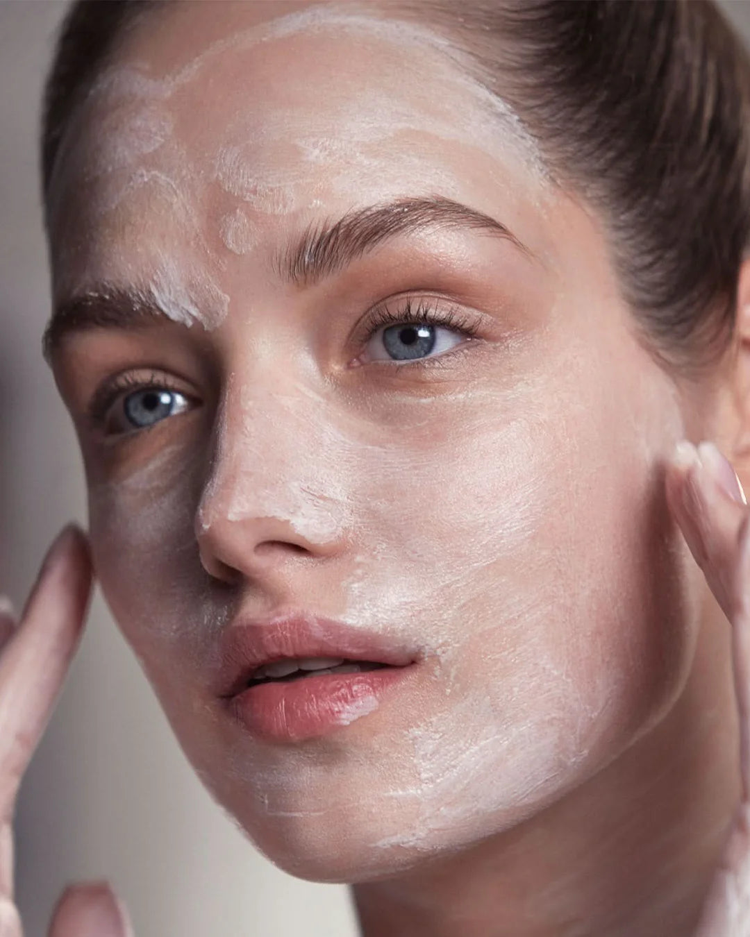 Close-up of a person applying a white cream or mask to their face.