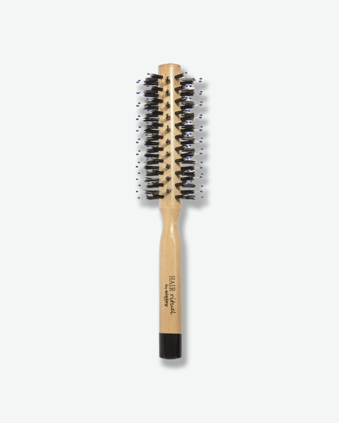 A top-down view of a HAIR Rituel by Sisley round blow-dry hairbrush, featuring a natural light-wood body and handle, dense black bristles mixed with blue ball-tipped pins, and a black base cap.
