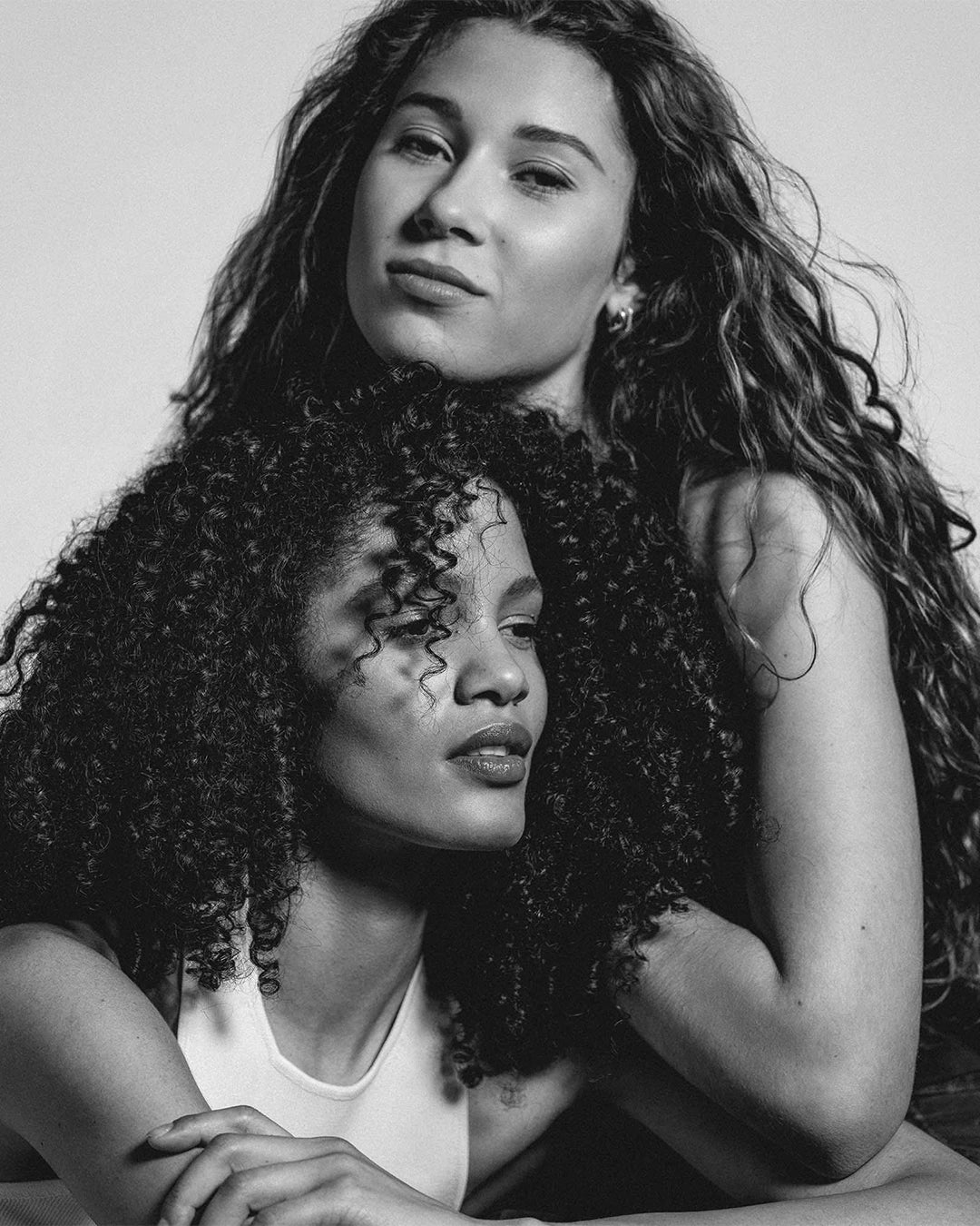 Black and white photo of two women with curly hair embracing each other.