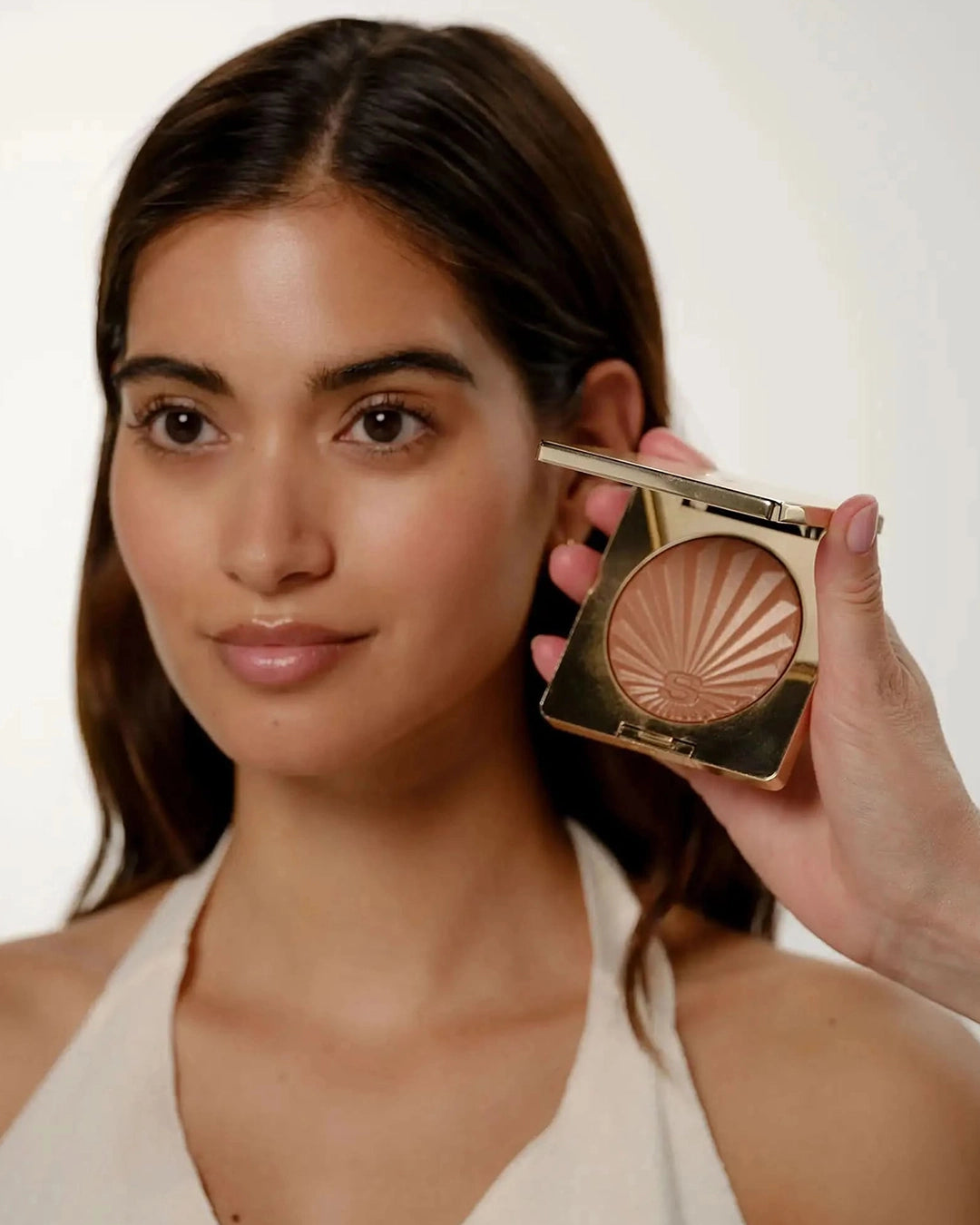 Woman holding a compact powder with a neutral background