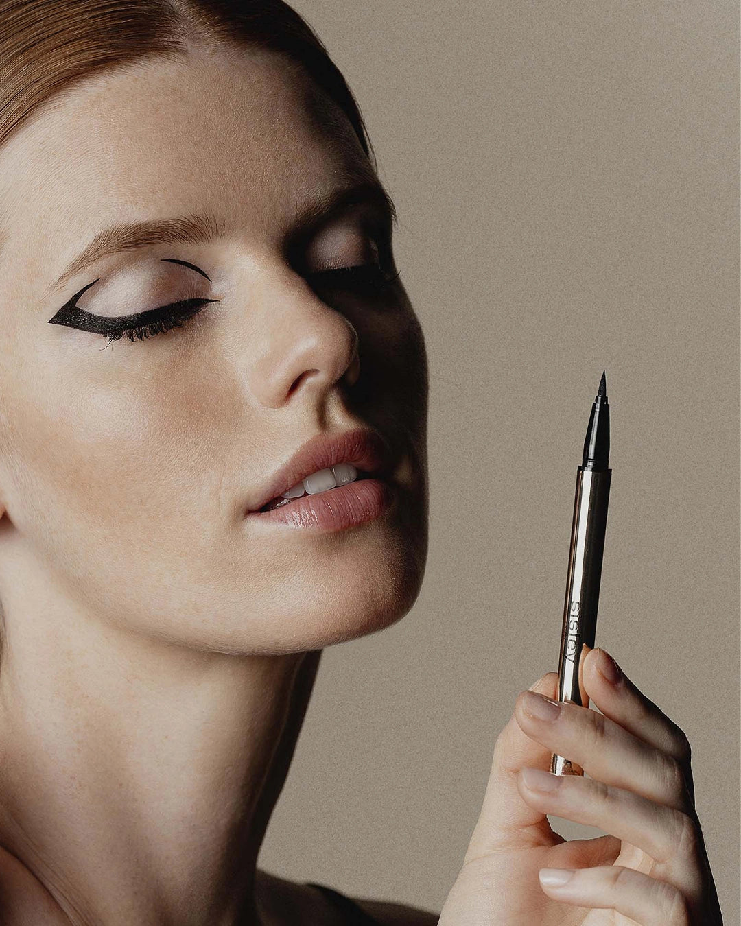 Woman holding a eyeliner pen with a neutral background