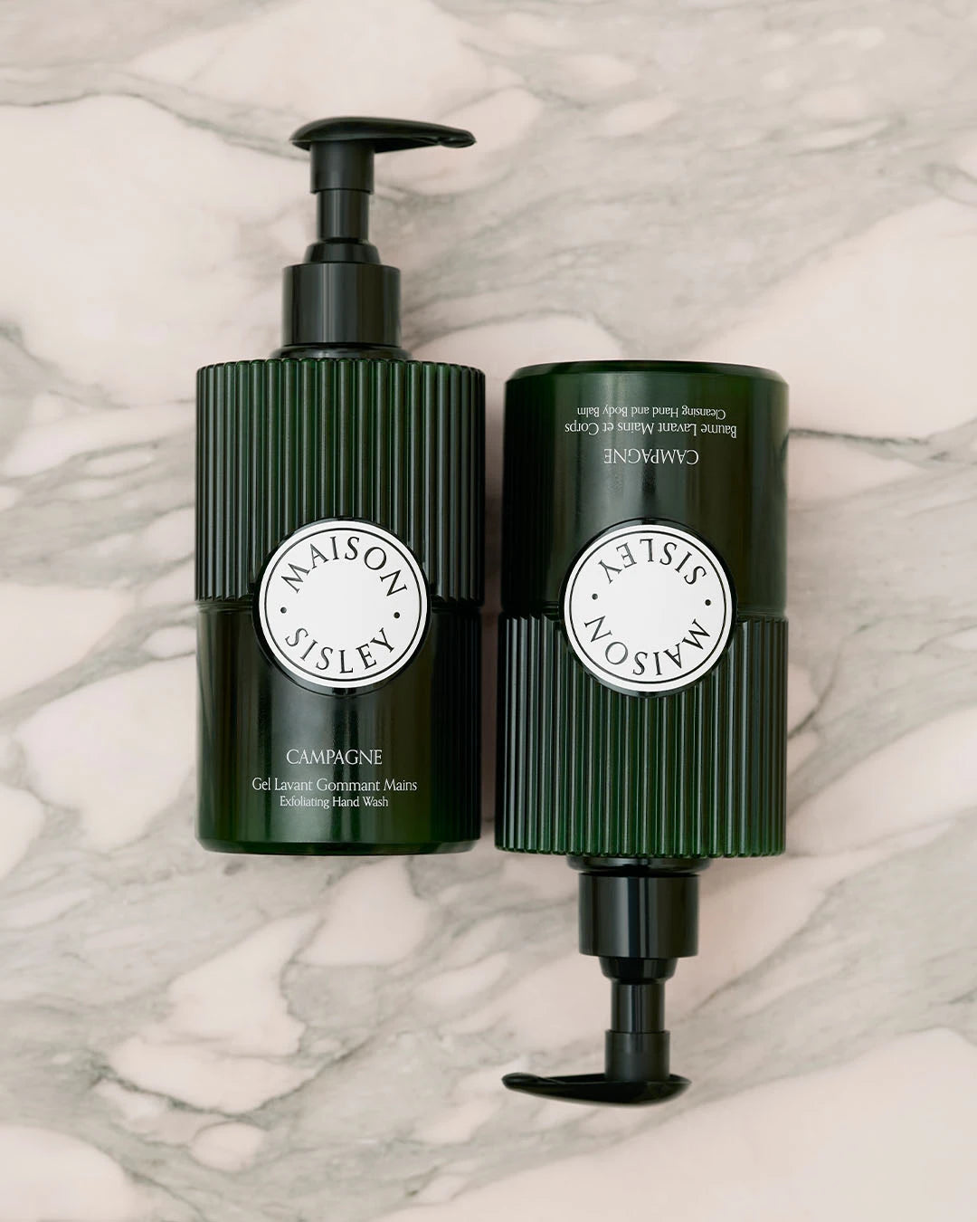 Two green bottles with pump dispensers on a marble surface, featuring the Maison Sisley brand.