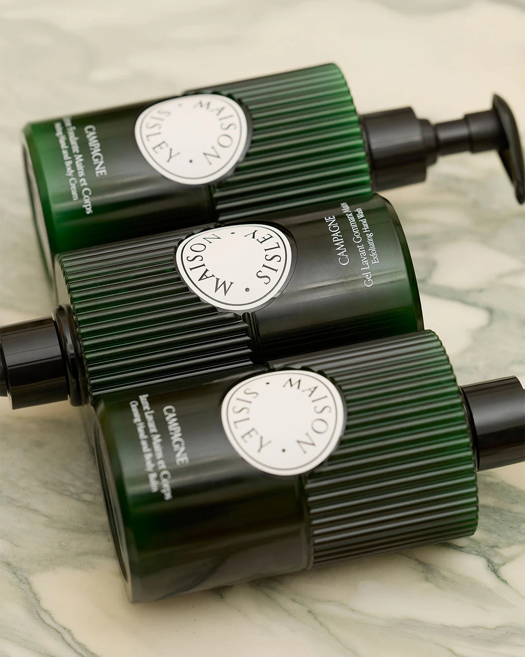 Three green skincare bottles with a visible brand logo on a marble surface