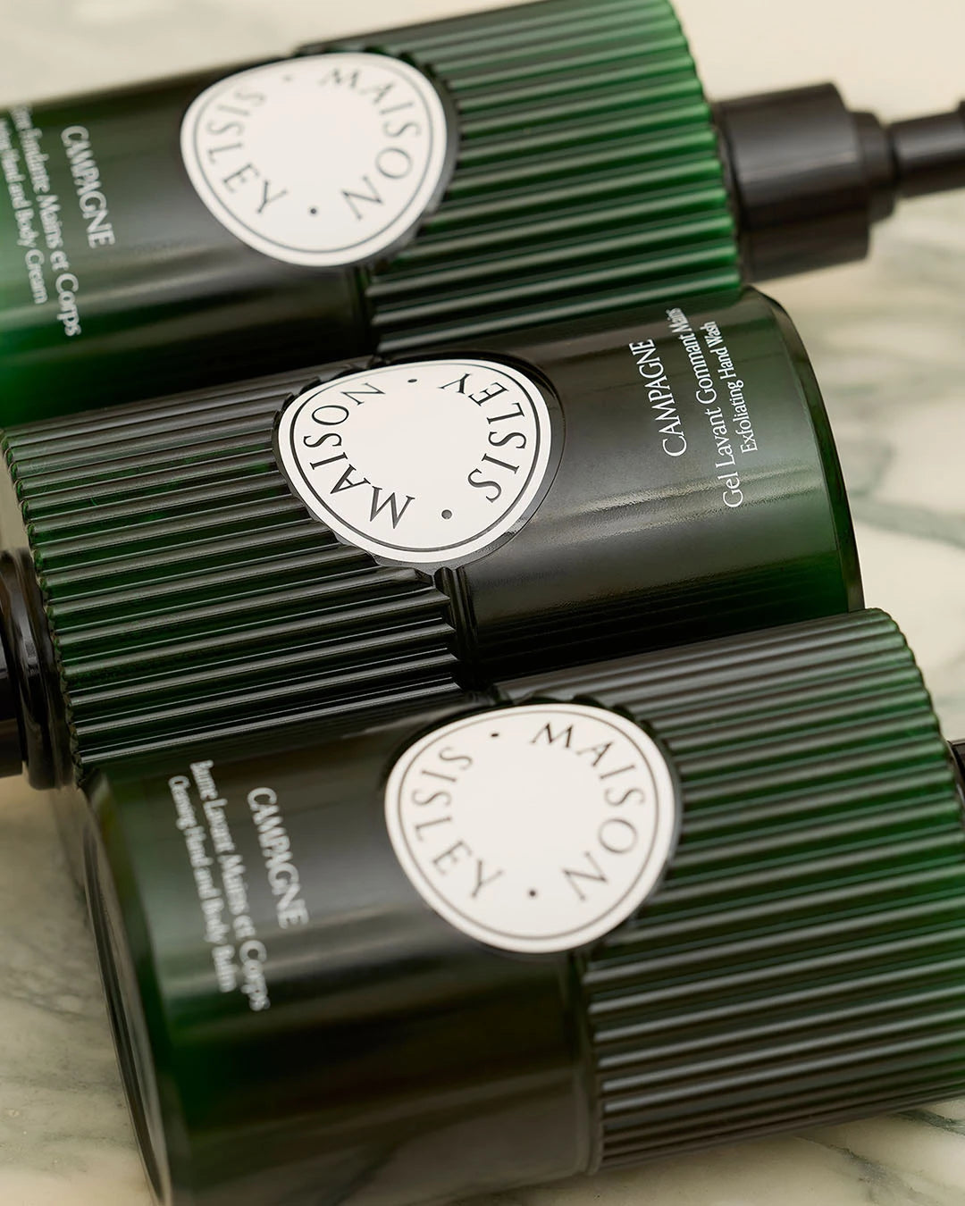 Three green skincare bottles with visible branding on a marble surface
