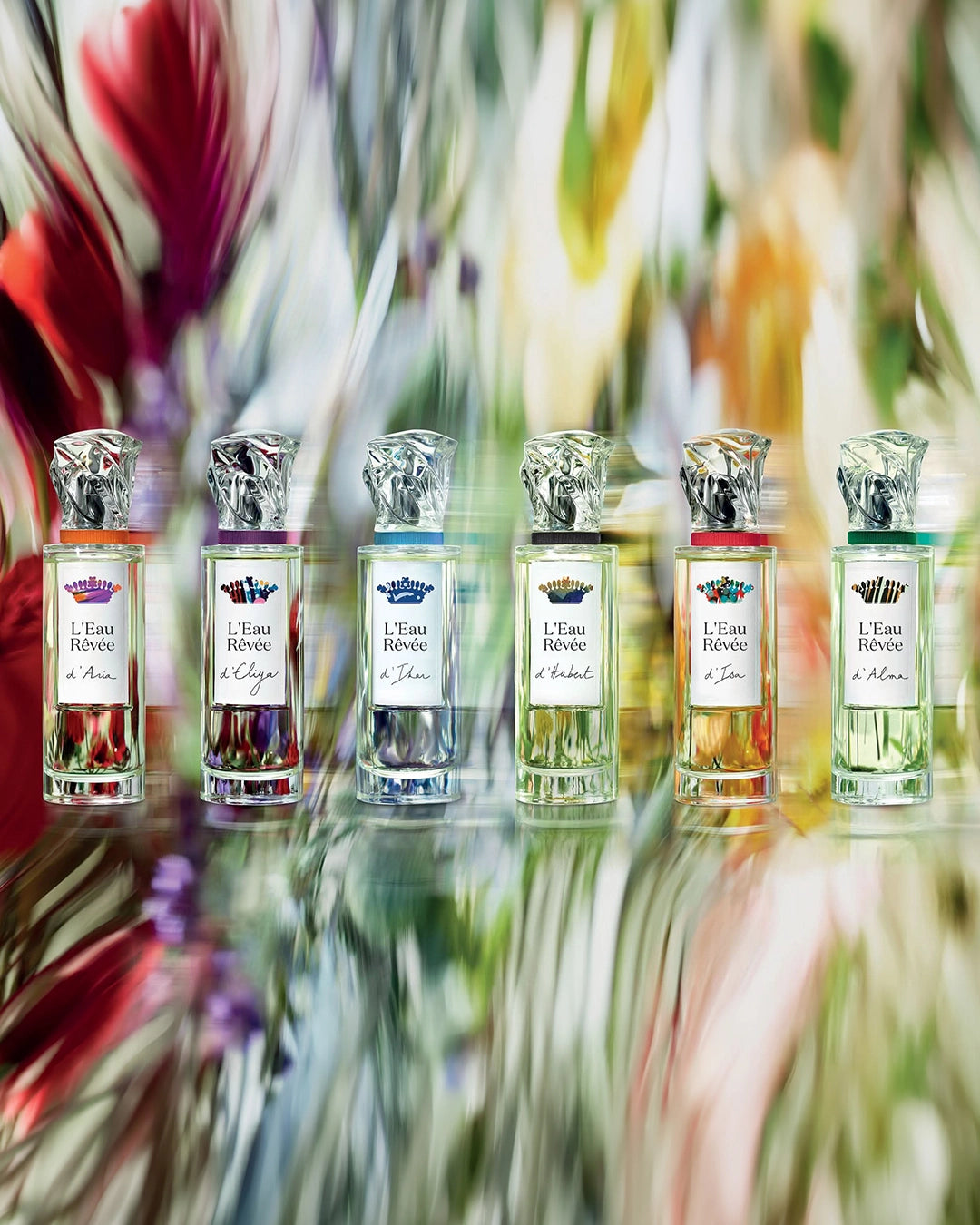 Set of perfume bottles labeled 'L'Eau Revee' on a reflective surface with floral background