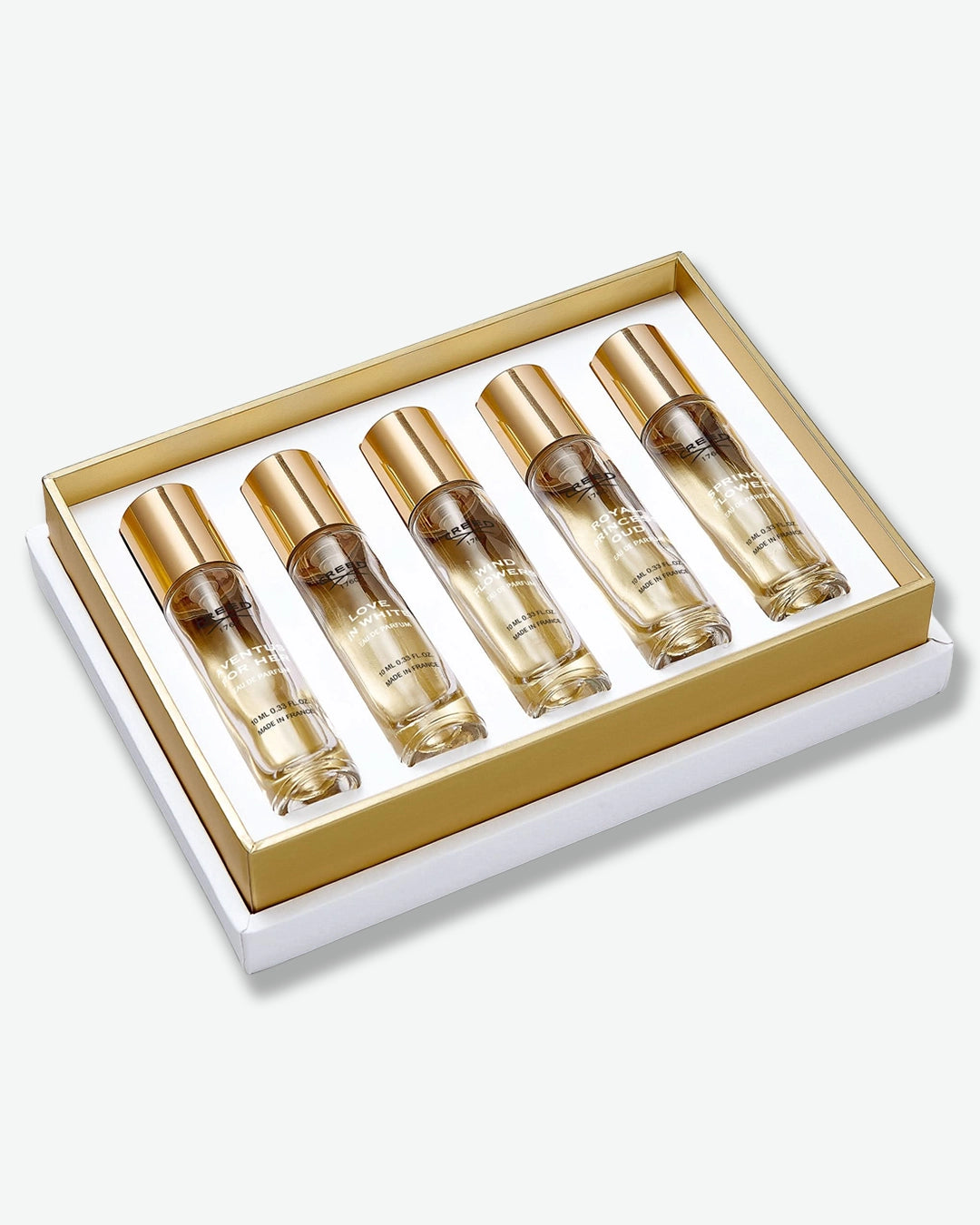 Alternate diagonal view of the Creed luxury perfume gift set shown from a top-down view. Nestled in a gold-bordered white tray, are five identical clear glass travel spray bottles with gold caps. From left to right, the bottles are labeled "Aventus for Her", "Love in White", "Wind Flowers," "Royal Princess Oud," and "Spring Flower," each marked as 10 ml Eau de Parfum made in France.
