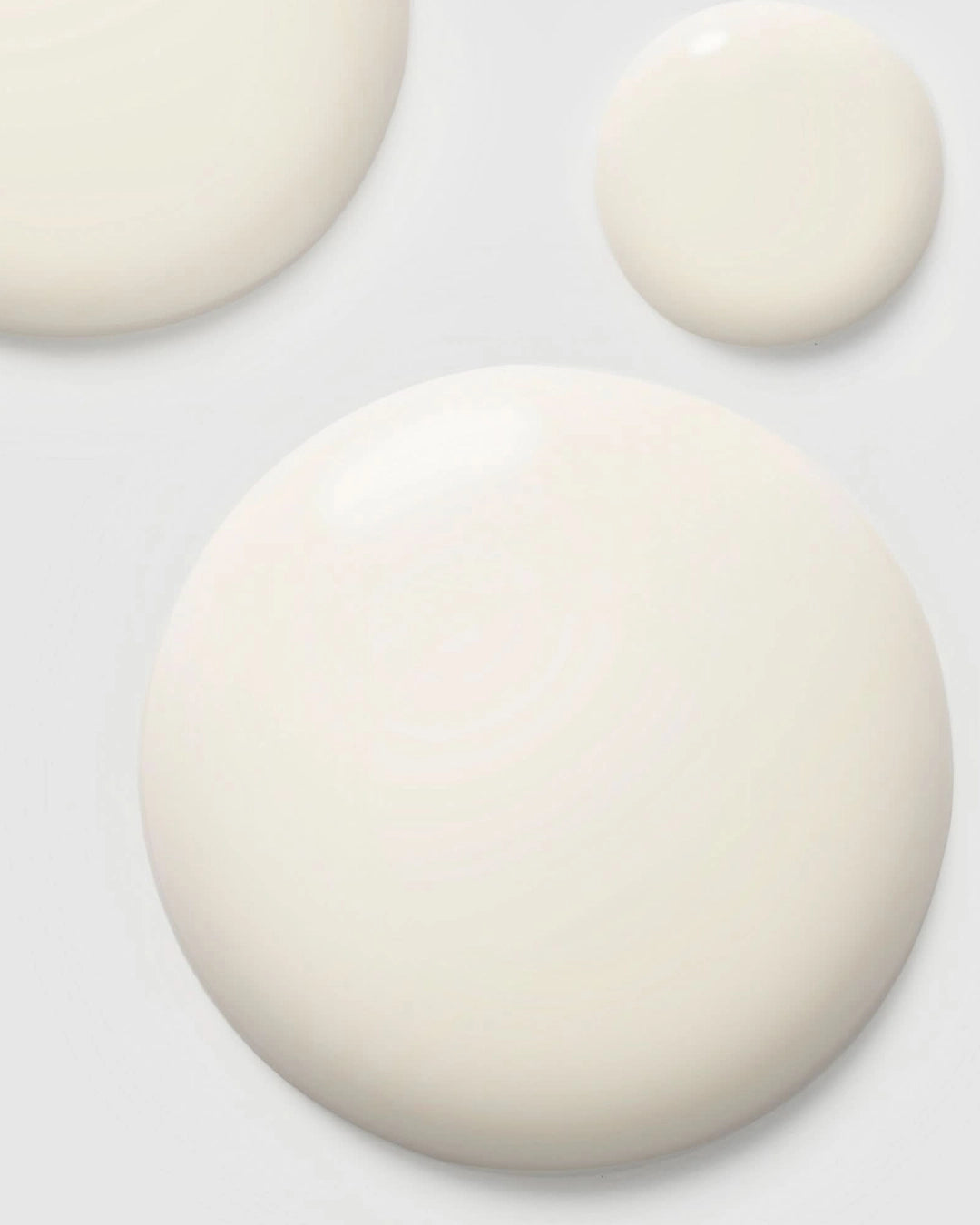 Close-up of three white drops of serum on a light gray background