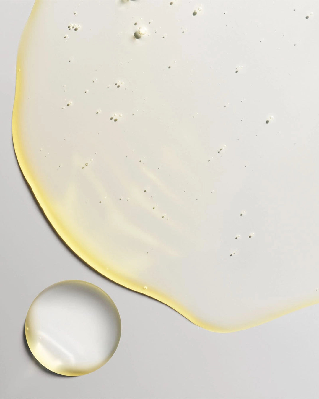 Close-up of a yellow gel-like substance with a droplet on a light gray background