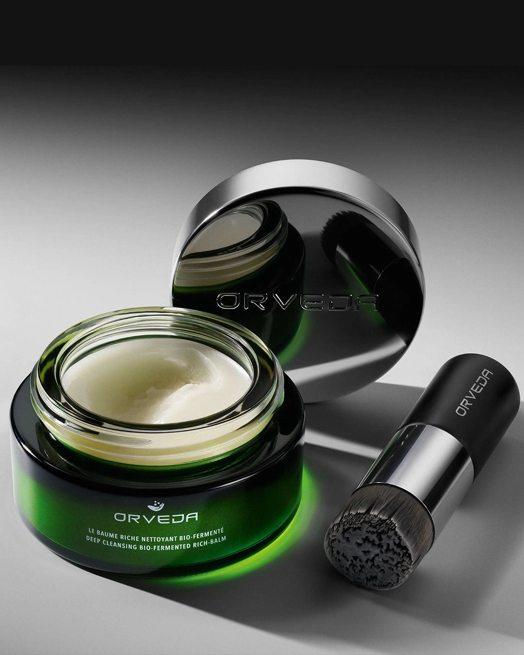 Orveda skincare product with jar, brush, and packaging on a gray background