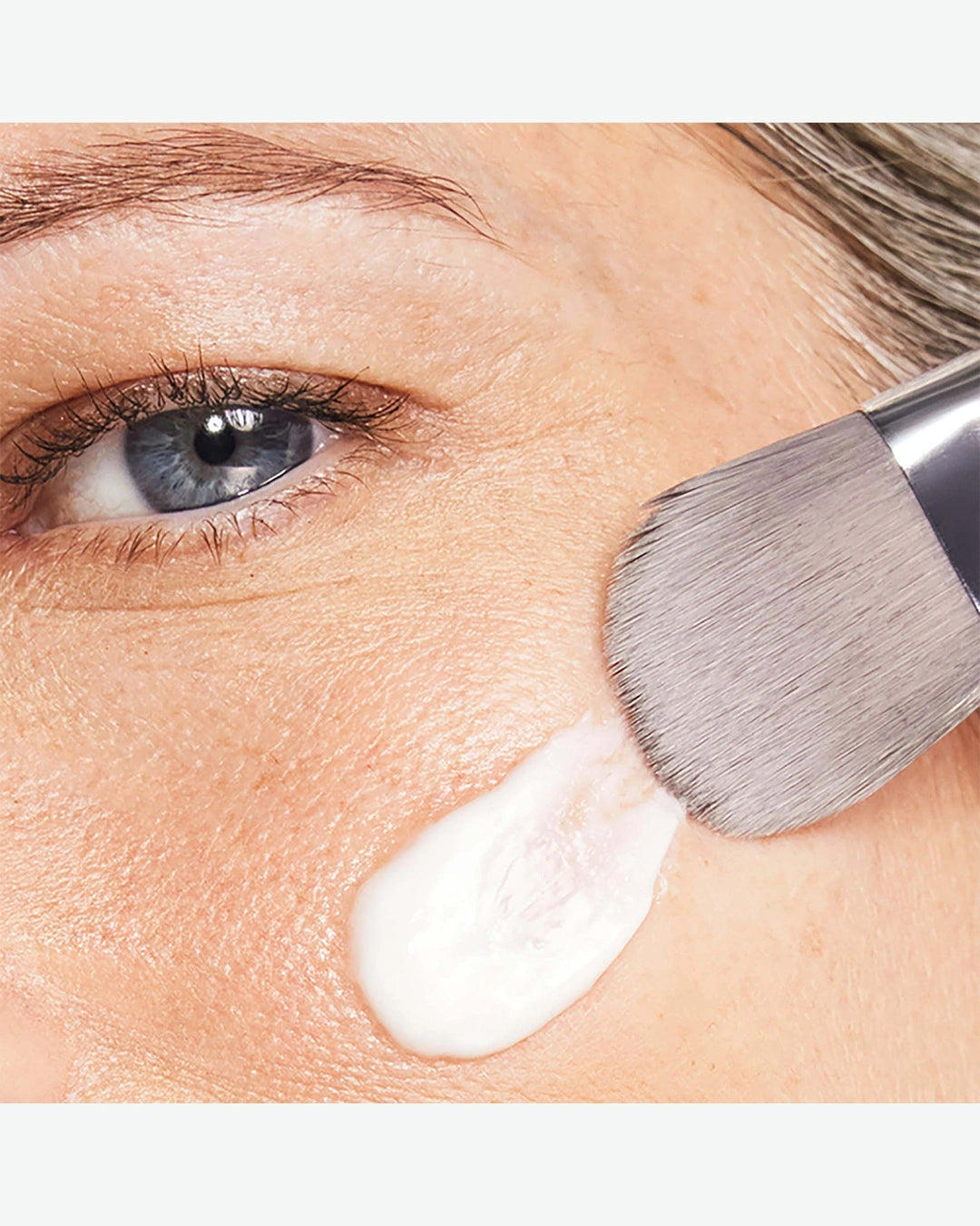 Person applying white cream to face with a brush