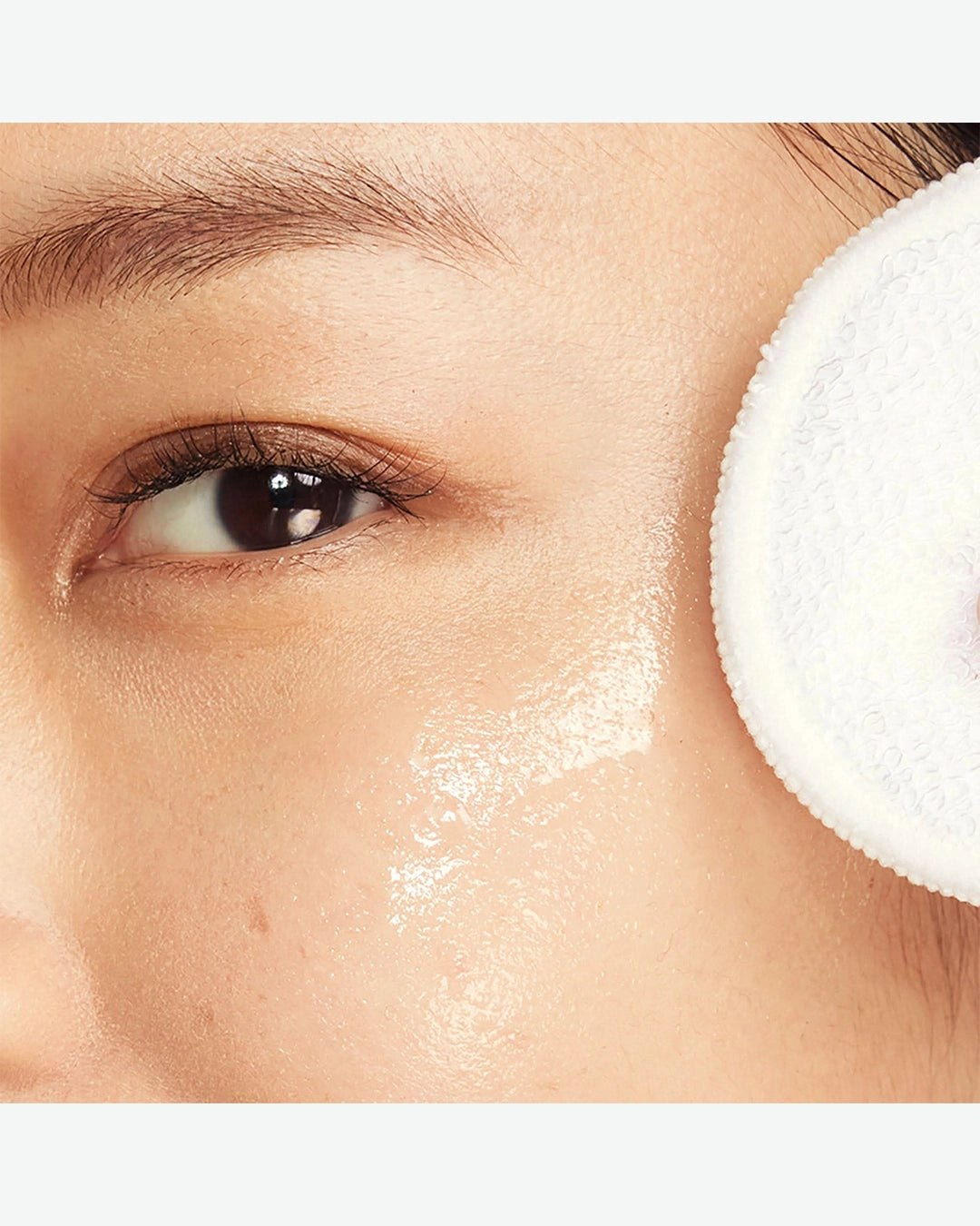Close-up of a person applying a skincare product with a white applicator to their face.