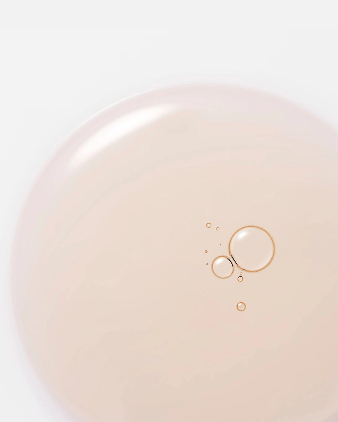 Close-up of a beige serum with gold bubbles on a light pink background