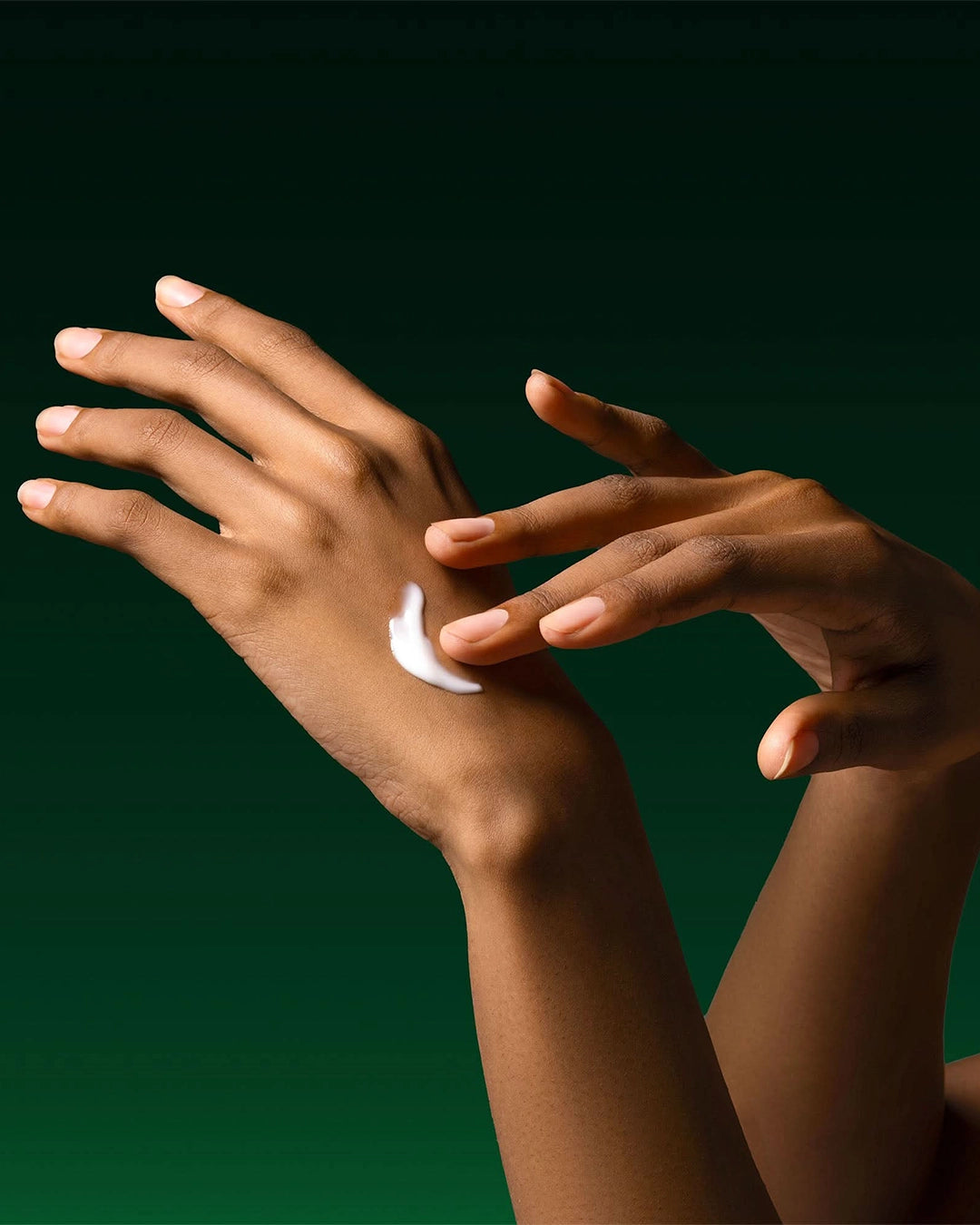 Two hands with a small amount of cream on one palm against a dark green background