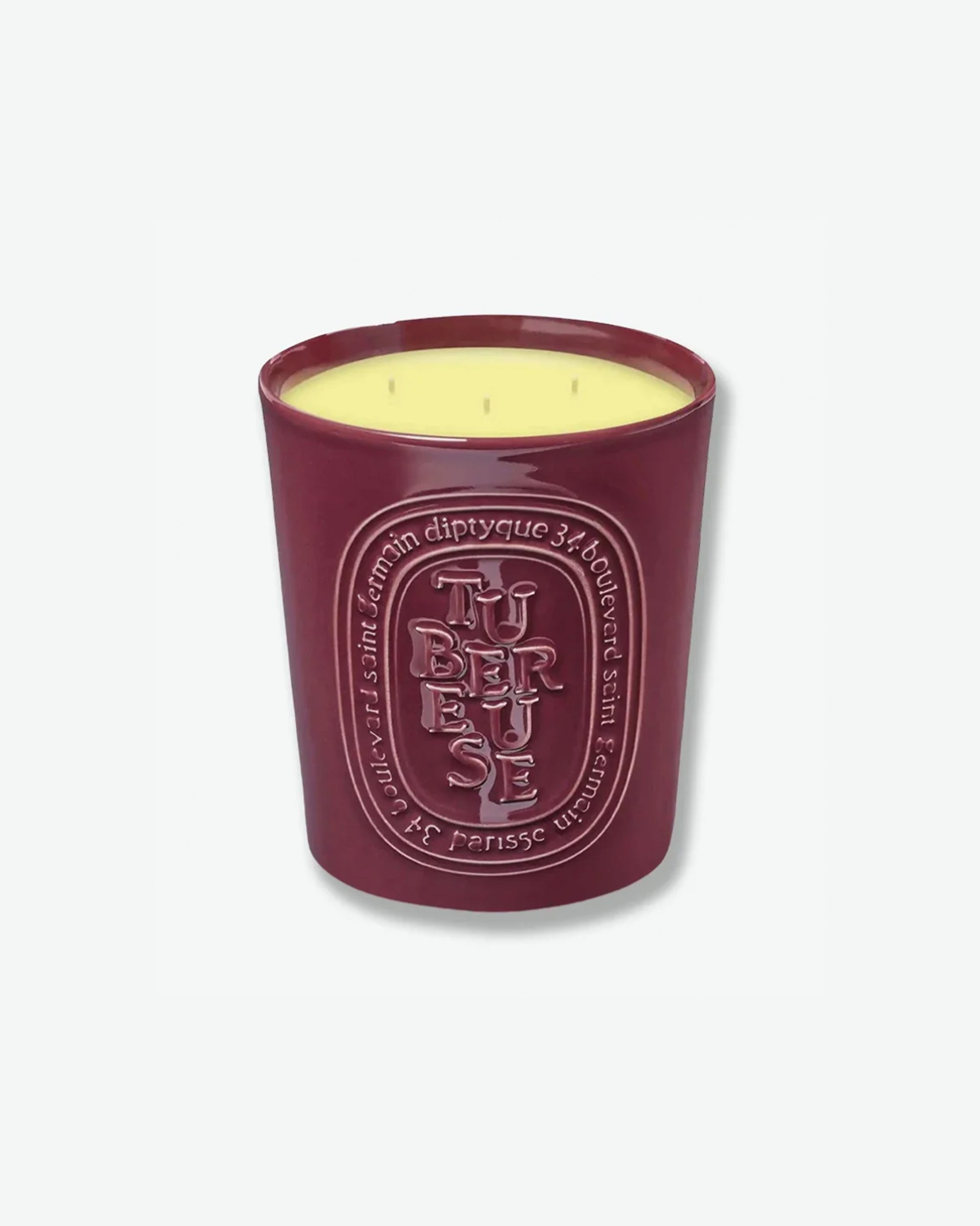 Diptyque Tubéreuse multi-wick scented candle in a glossy, dark plum-colored ceramic vessel featuring an embossed oval logo, isolated on a light grey background.