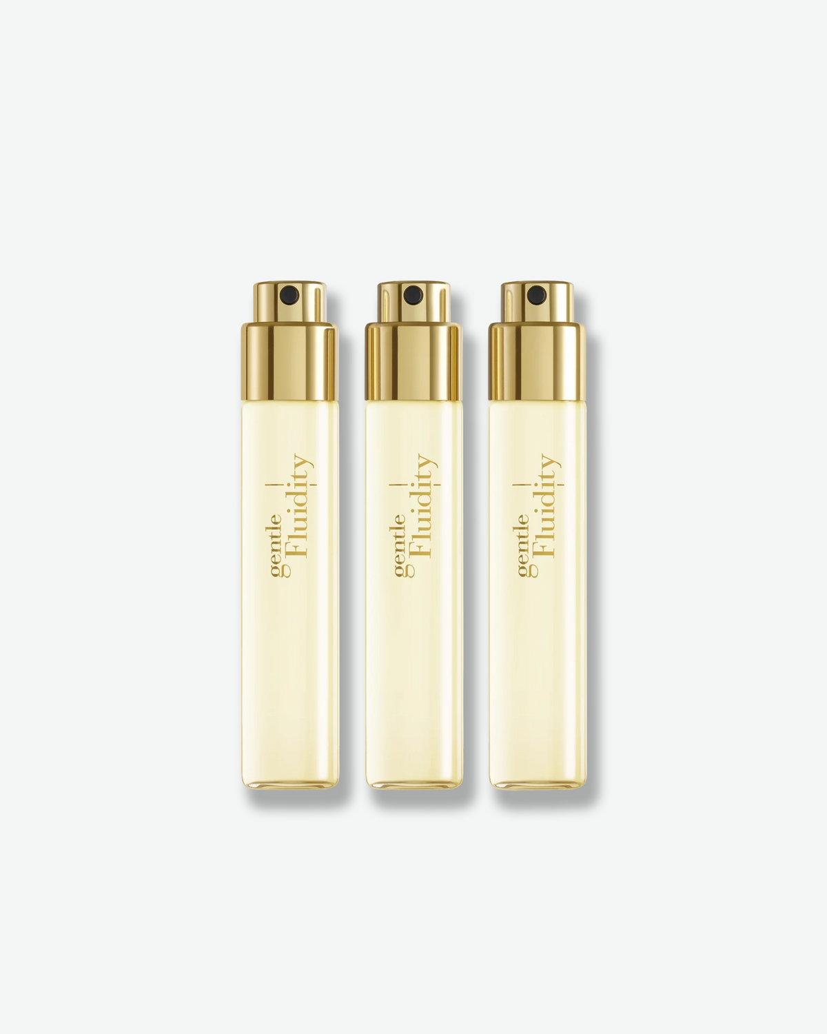 Three Gentle Fluidity Gold Eau de Parfum travel spray bottles featuring pale golden fragrance, gold atomizers, and gold lettering against a white background.