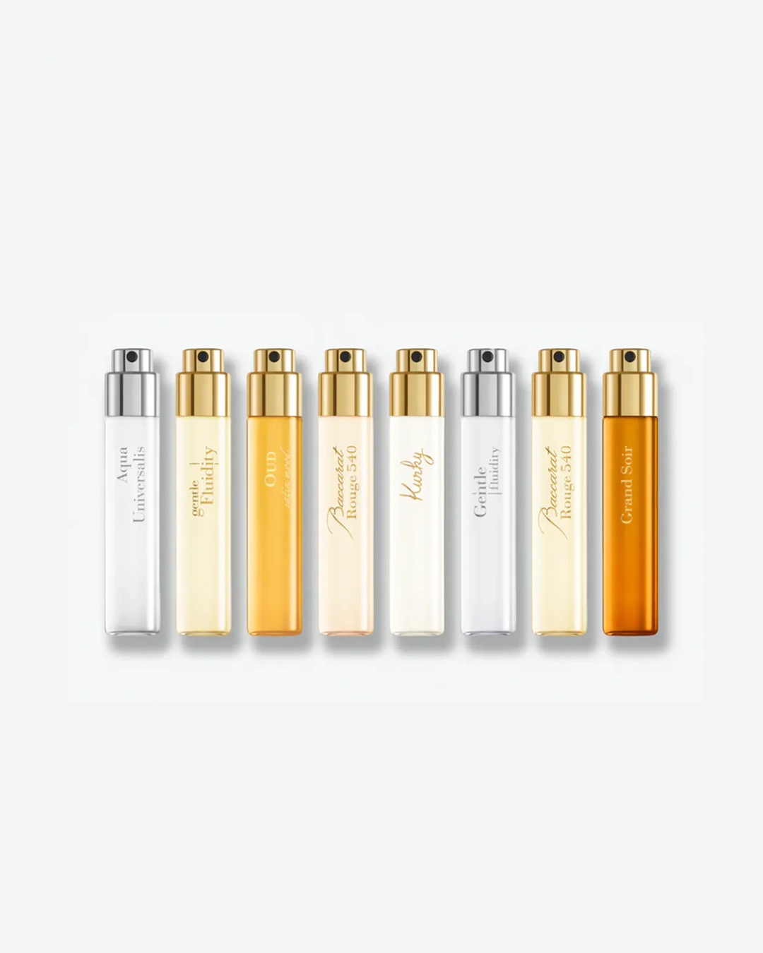 A row of eight Maison Francis Kurkdjian travel-sized fragrance spray vials arranged side by side against a plain white background, casting a soft shadow below. The glass vials feature a mix of gold and silver spray tops with distinct labels reading vertically from left to right: "Aqua Universalis" (silver top, clear liquid), "gentle Fluidity" (gold top, pale yellow liquid), "OUD silk mood" (gold top, amber liquid), "Baccarat Rouge 540" (gold top, light peach liquid), "Amyris" (gold top, clear liquid), "Gent