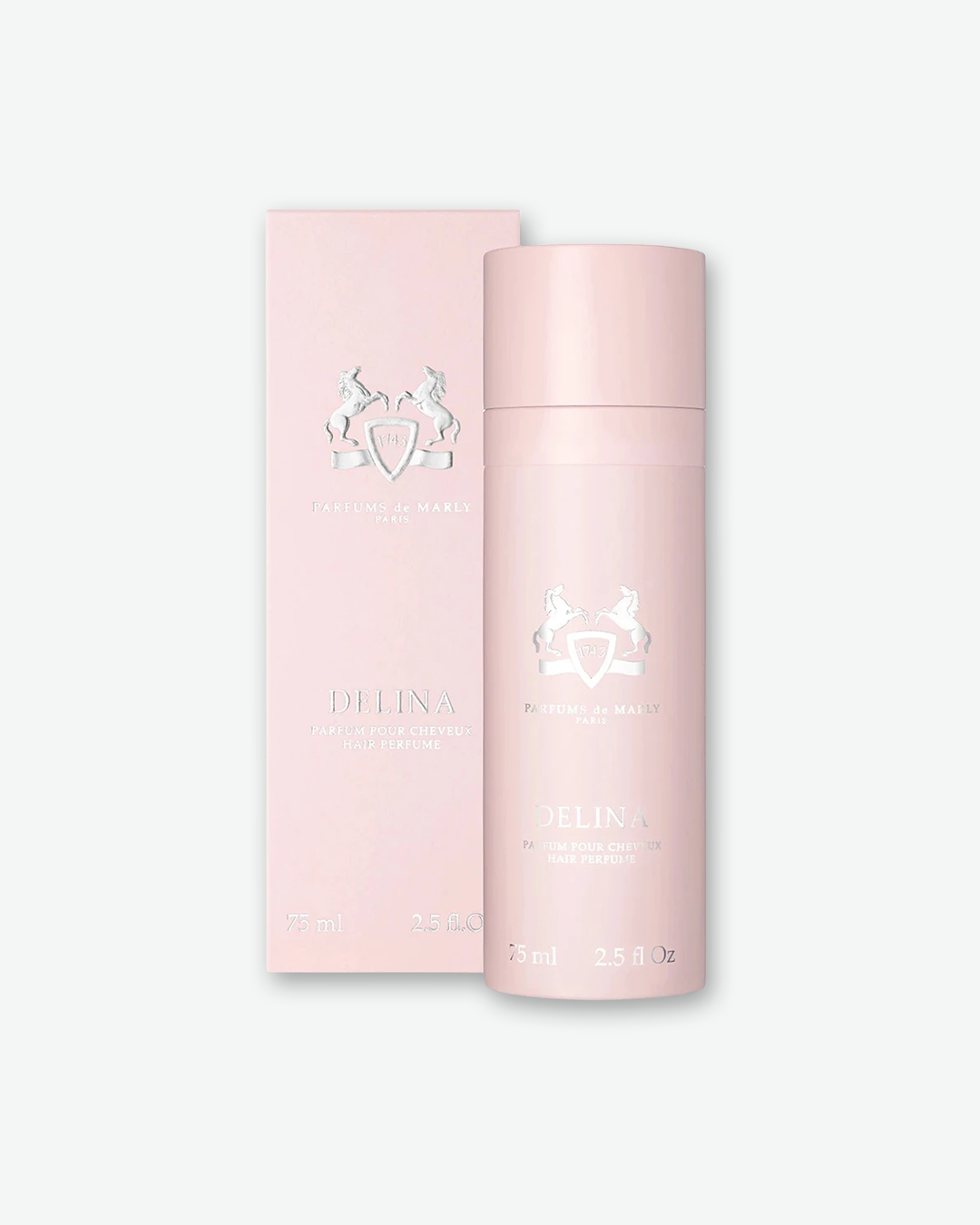 A product presentation shot showing a Parfums de Marly Delina Hair Perfume bottle standing in front of its soft pink packaging box. Both items display matching silver embossed brand details, featuring the iconic equestrian crest logo, brand name, and 'DELINA HAIR PERFUME' centered on a clean, pastel pink background.