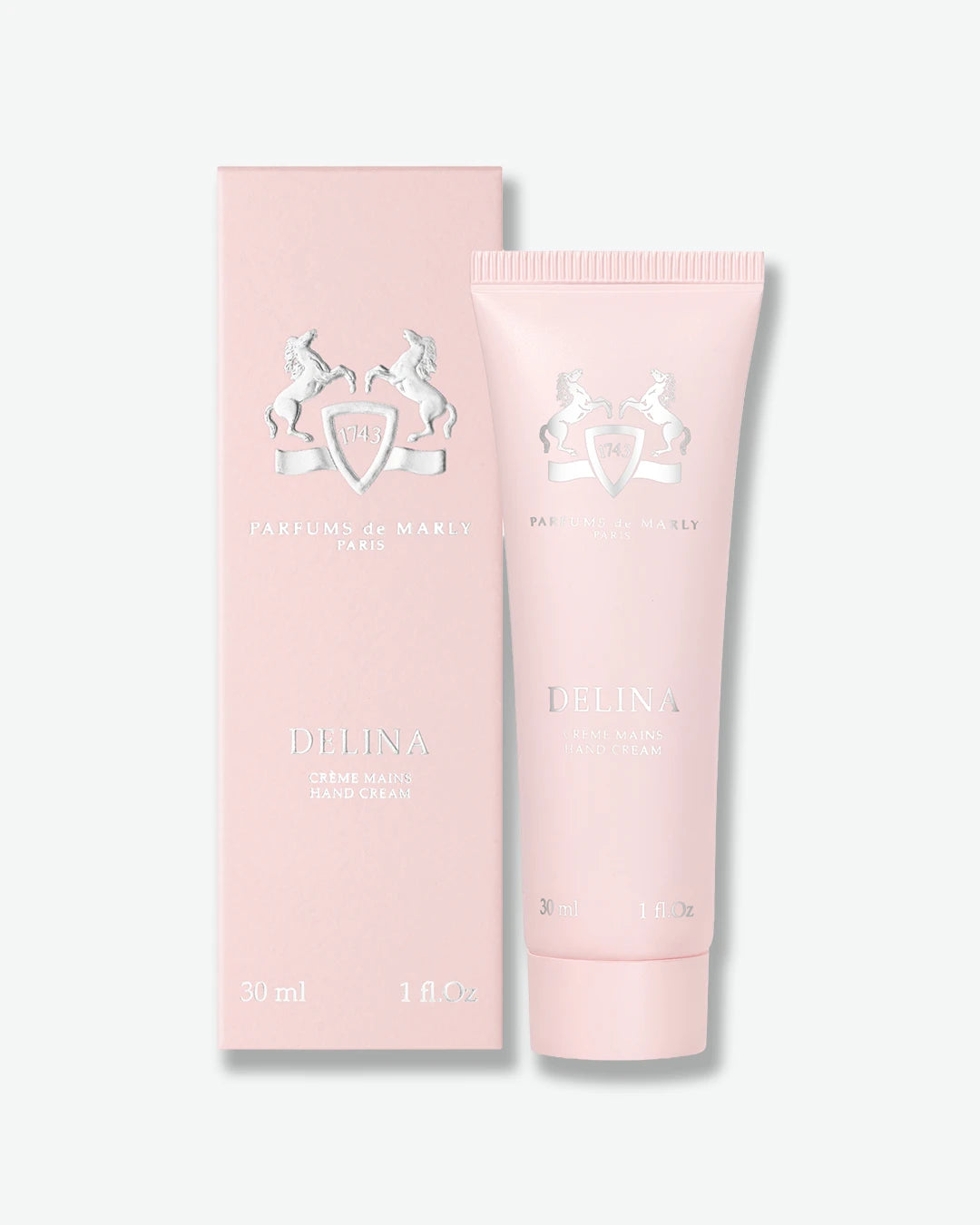A light pink tube of Delina Hand Cream next to its matching pink packaging box, both featuring silver foil branding, on a clean off-white background.