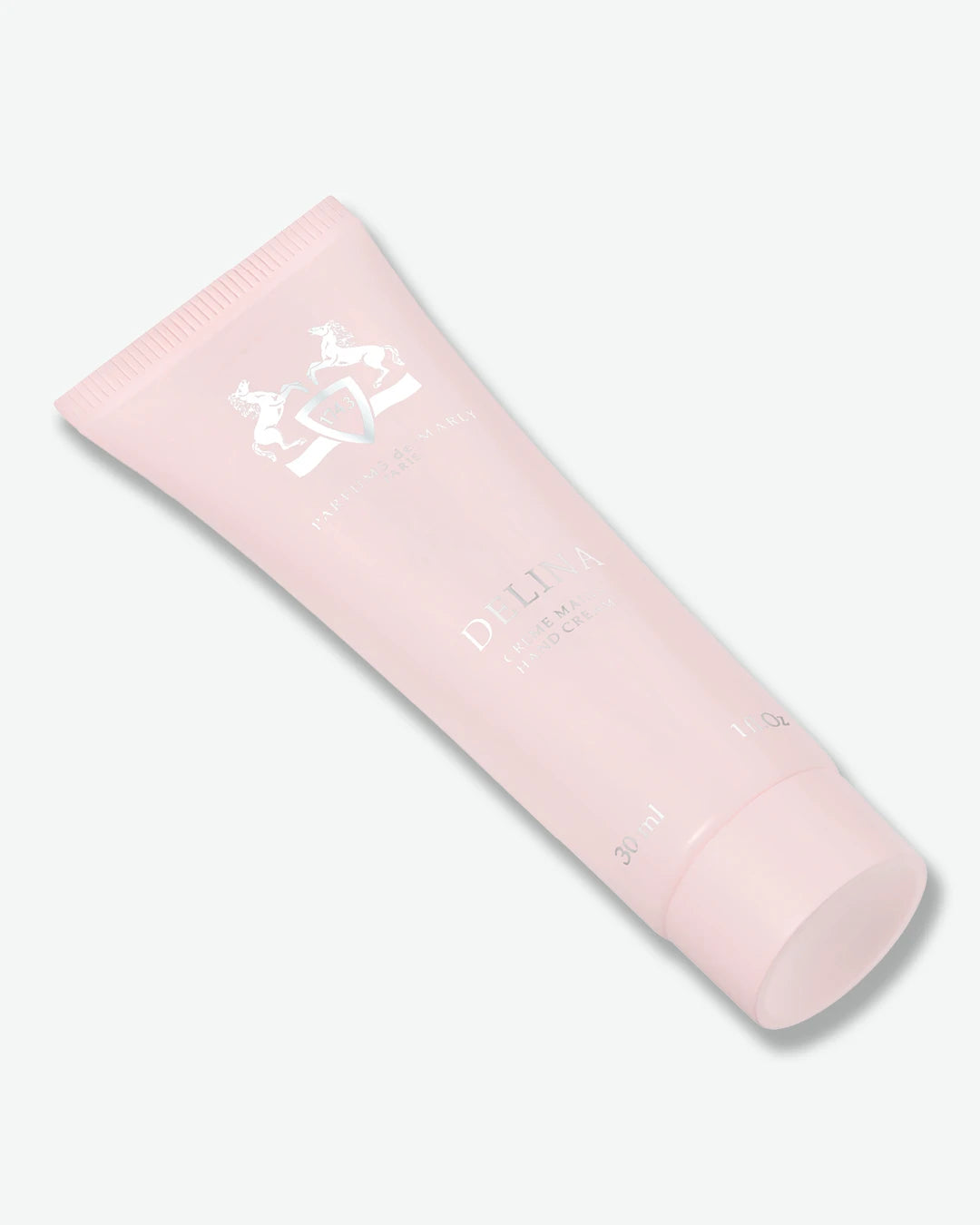A light pink squeeze tube of Delina Hand Cream by Parfums de Marly, shown diagonally on a clean, light off-white background.