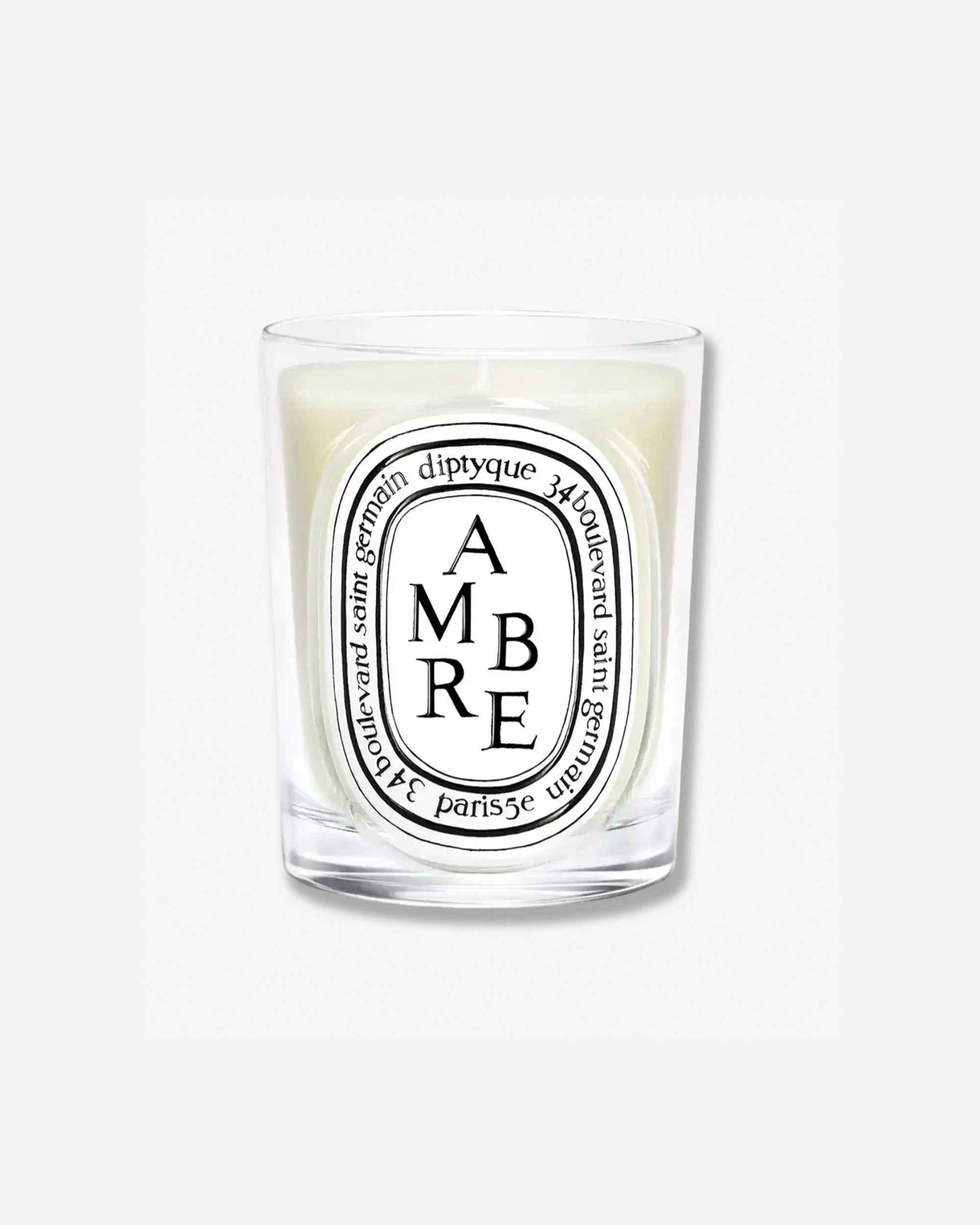 Diptyque Ambre scented candle in a classic clear glass jar featuring the signature white oval logo with black lettering, isolated on a light grey background.