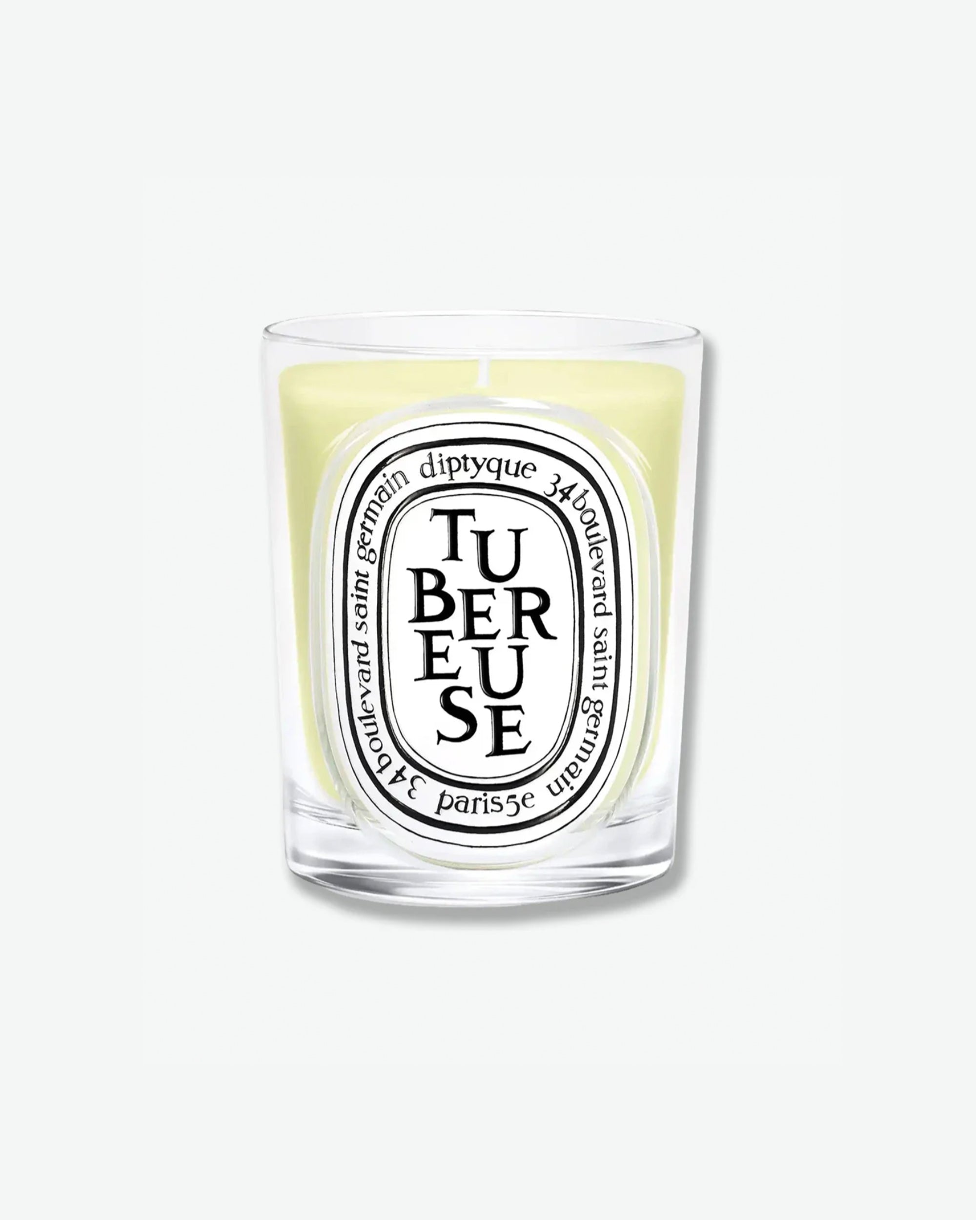 Diptyque Tubéreuse scented candle showcasing light yellow-tinted wax in a classic clear glass jar with the signature white oval logo, isolated on a light grey background.