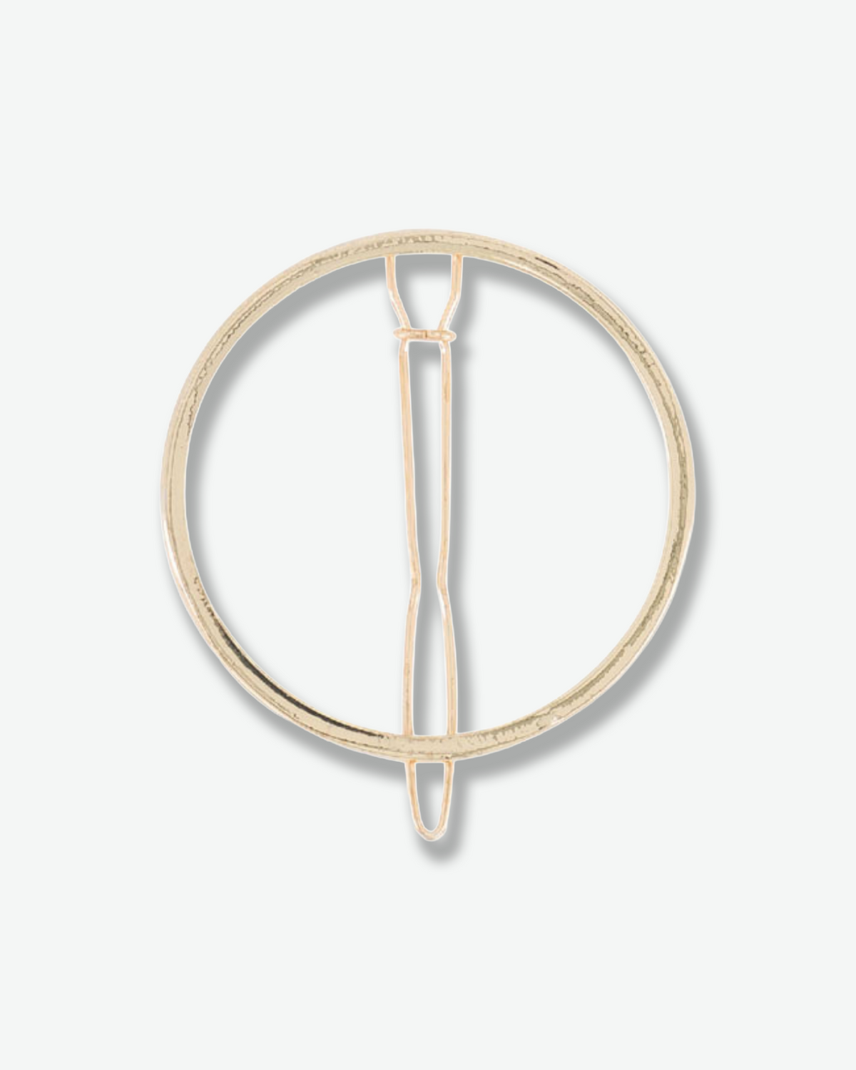 Minimalist circular gold-tone hair pin with a slender central fastening prong, displayed against a white background.