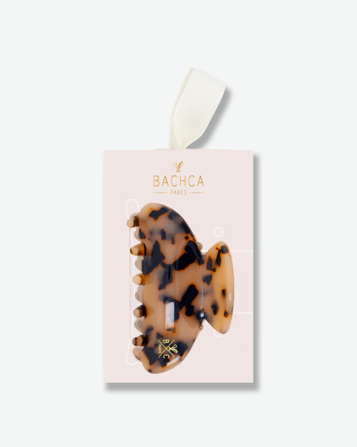 Tortoiseshell hair claw clip displayed on a pale pink Bachca Paris presentation card with gold lettering and an ivory ribbon.