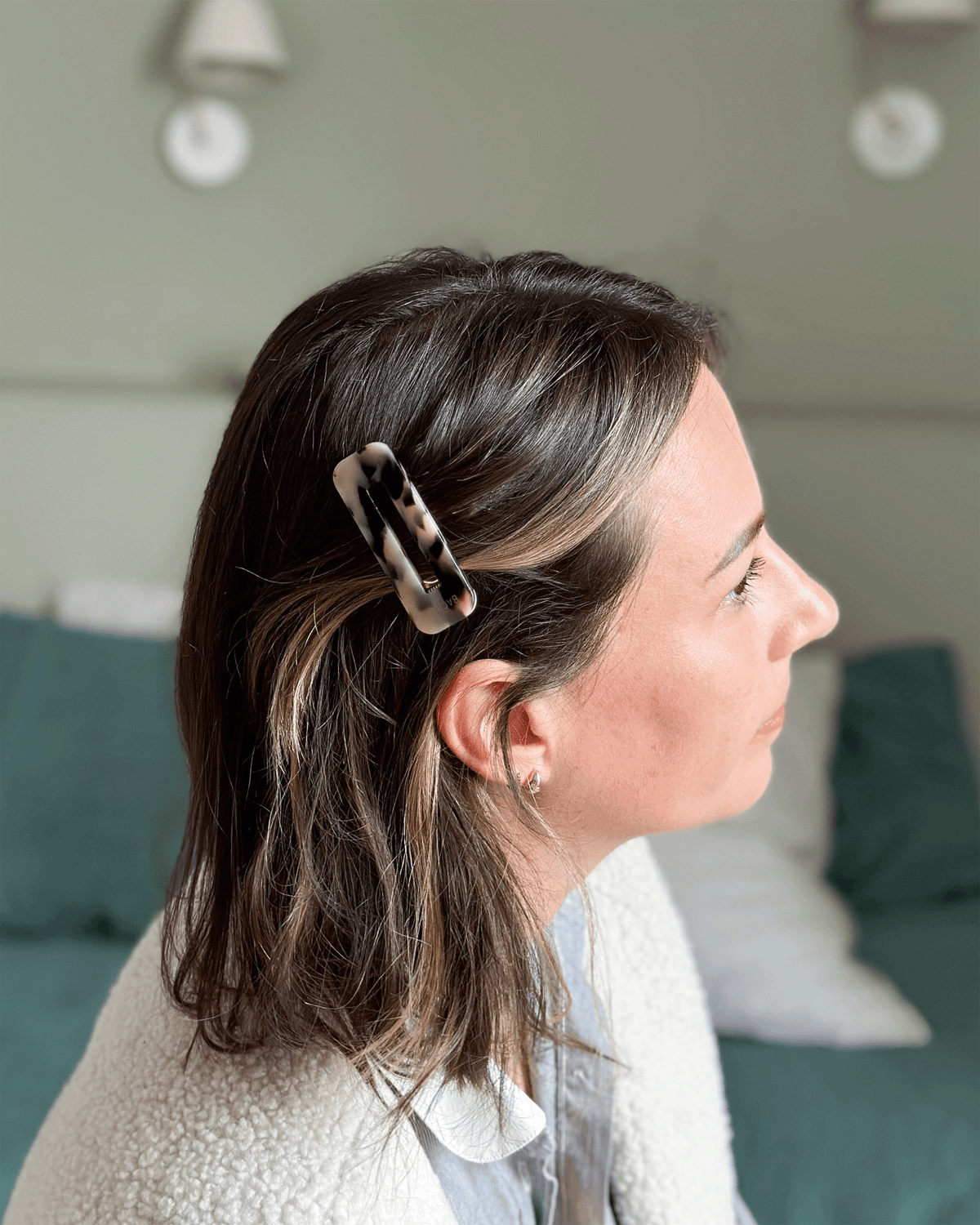 Side profile of a model with shoulder-length brown hair and blonde highlights, styled half-up with a rectangular tortoiseshell hair clip above her ear.
