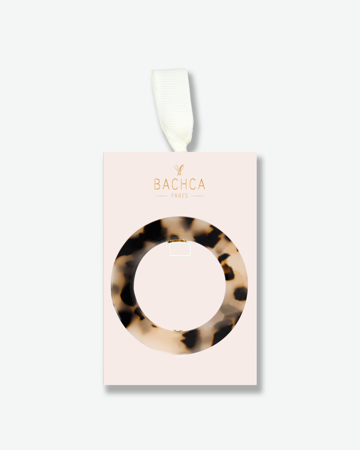 Circular tortoiseshell hair pin displayed on a pale pink Bachca Paris presentation card with gold lettering and an ivory ribbon.