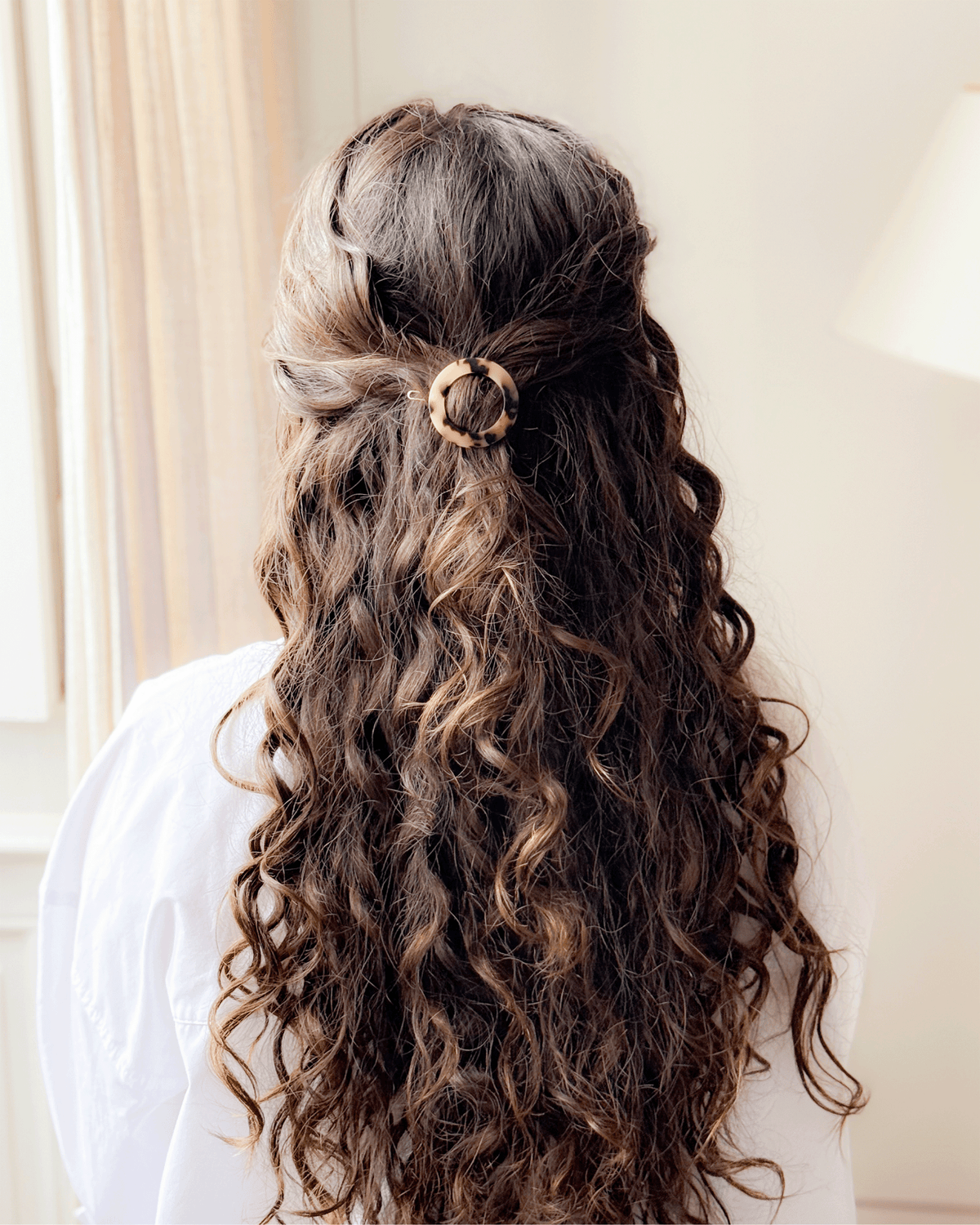 Rear view of a model with long, curly brown hair styled half-up and secured with a circular tortoiseshell Bachca Paris hair pin.