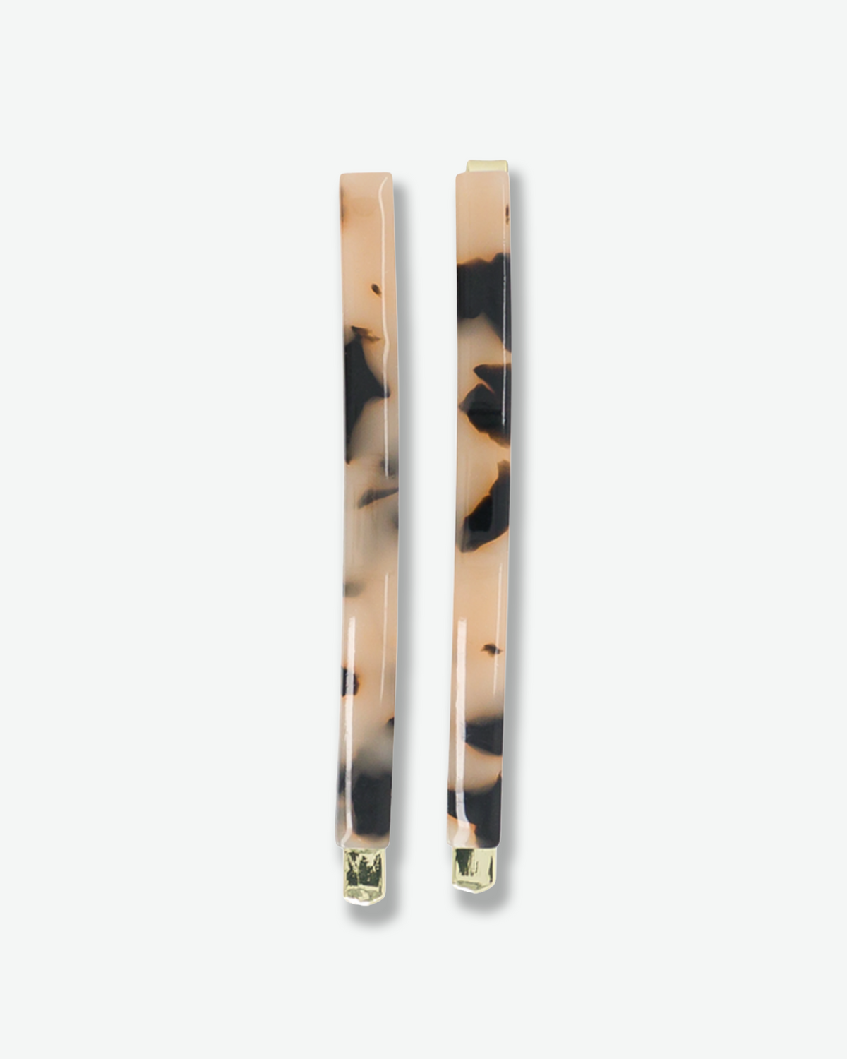 Two slim tortoiseshell hair clips featuring beige, brown, and black marbled patterns with gold-tone metal accents, displayed against a white background.