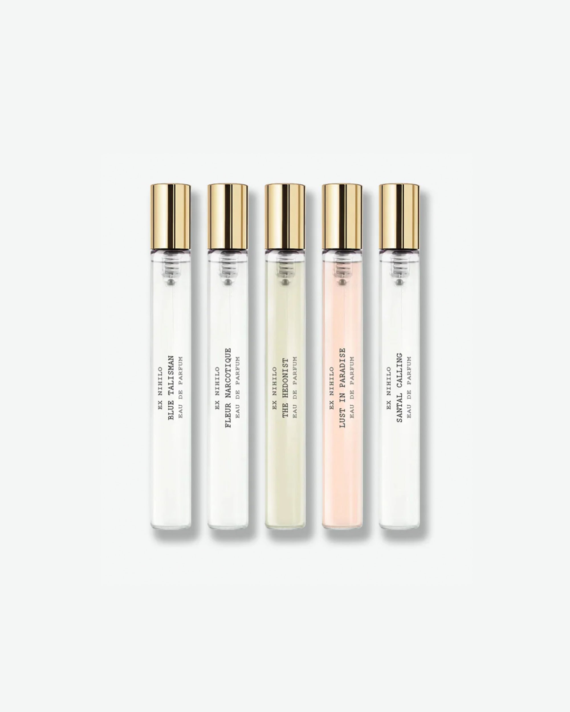 An Ex Nihilo fragrance discovery set displaying five travel spray vials with gold caps, featuring a variety of scents including Blue Talisman, Fleur Narcotique, The Hedonist, Lust in Paradise, and Santal Calling, isolated on a light grey background.