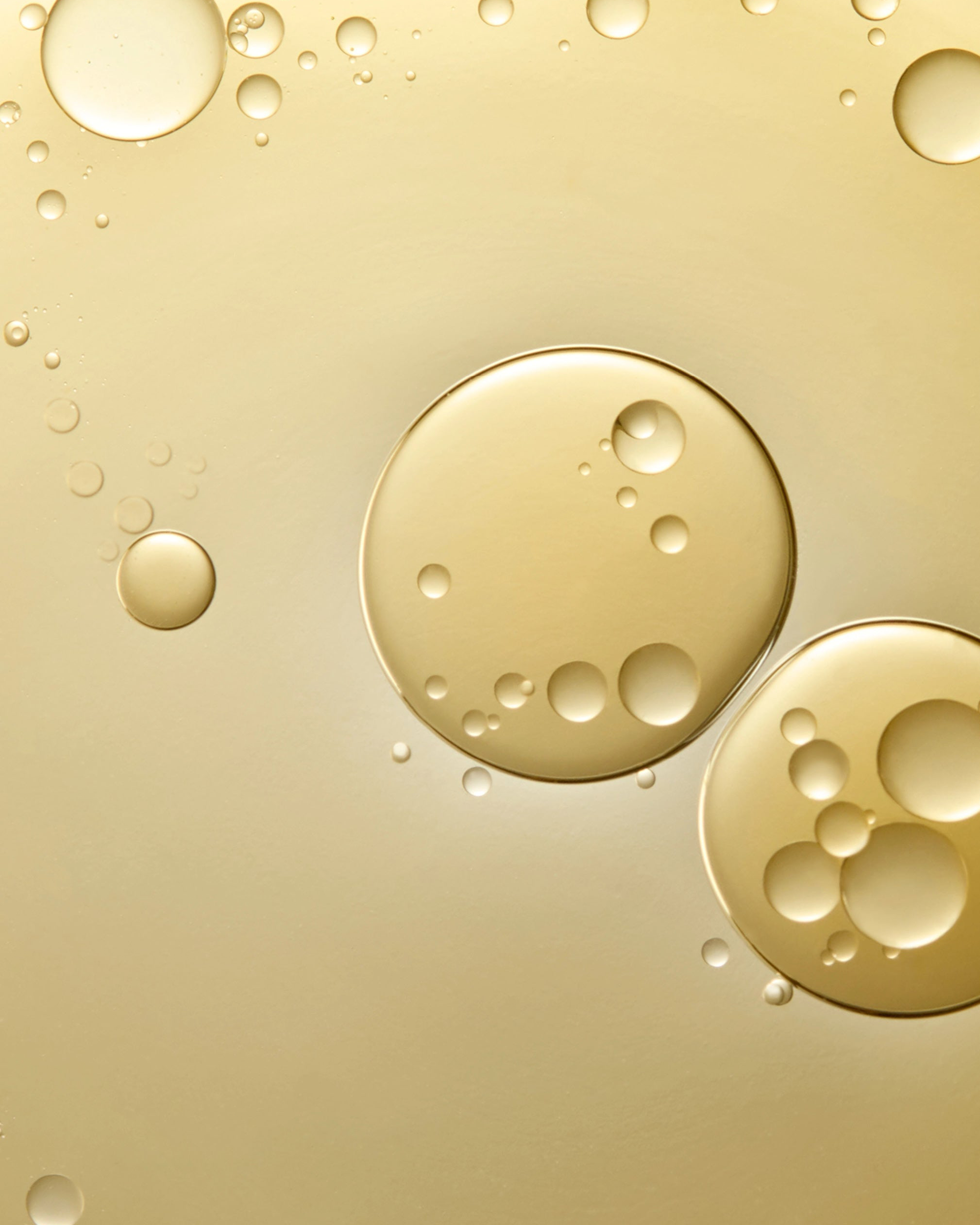 A close-up abstract view of translucent golden liquid droplets and bubbles on a warm gold background.
