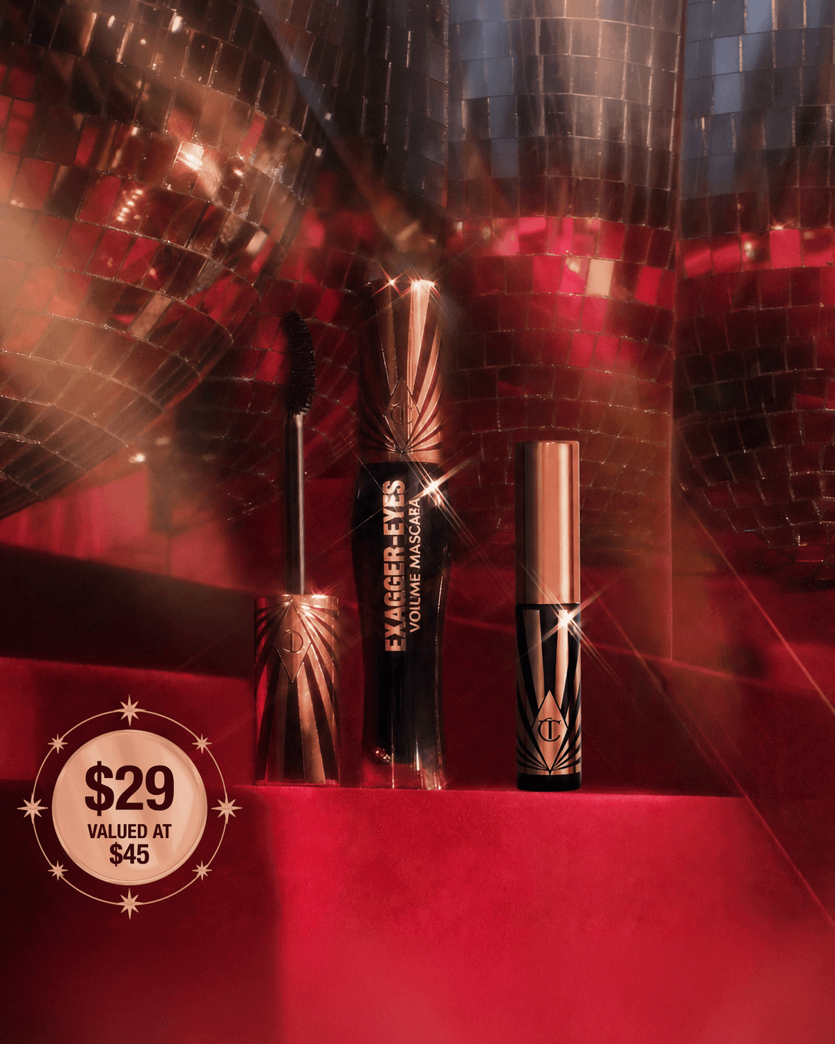 Charlotte Tilbury Exagger-Eyes Volume Mascara and mini mascara displayed against a red holiday backdrop with mirrored disco balls.