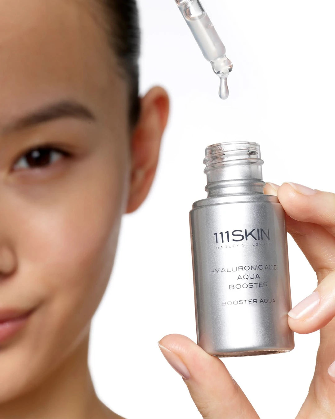 111SKIN skincare product with dropper held by a hand, close-up of face.