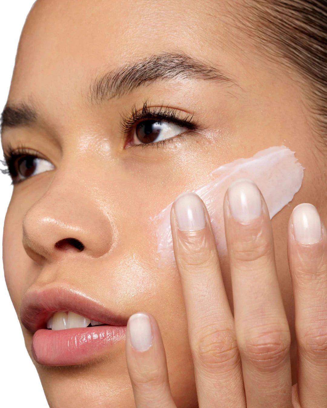 Close-up of a woman applying cream to her face with a white background