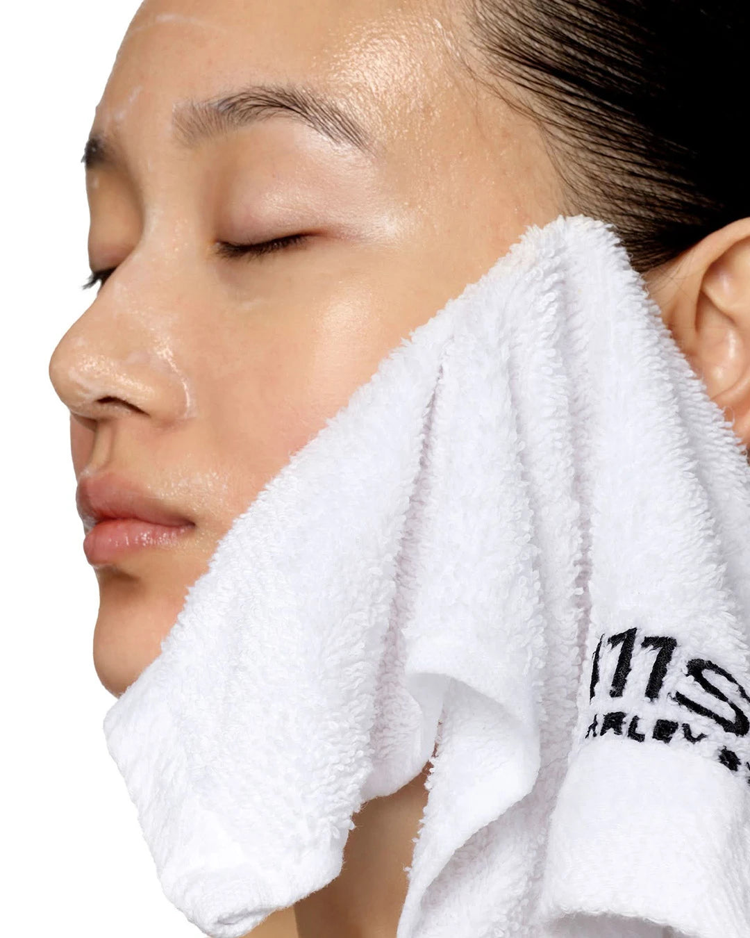 Person using a white towel on their face with a brand logo.
