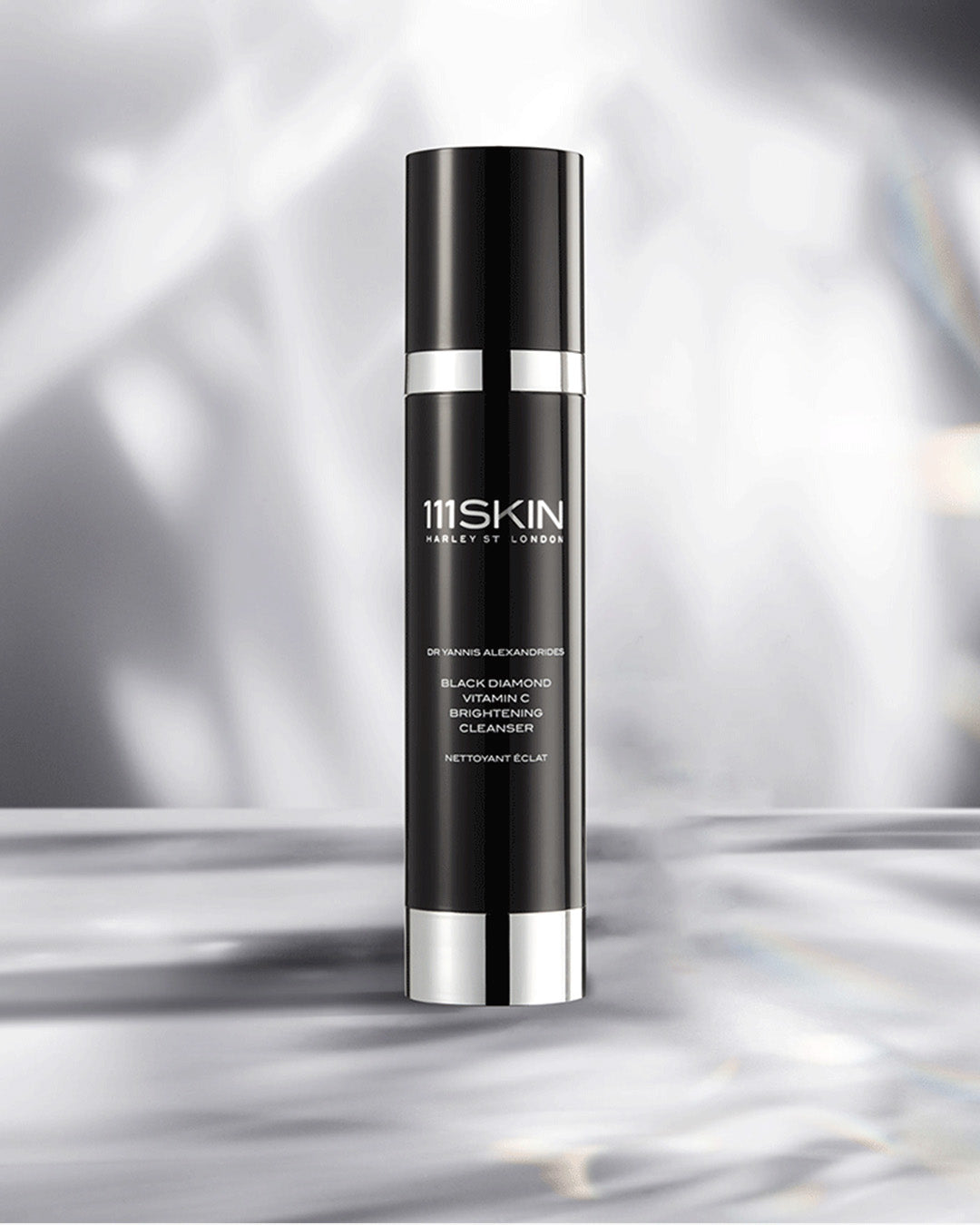 Black skincare bottle with silver accents on a reflective silver background