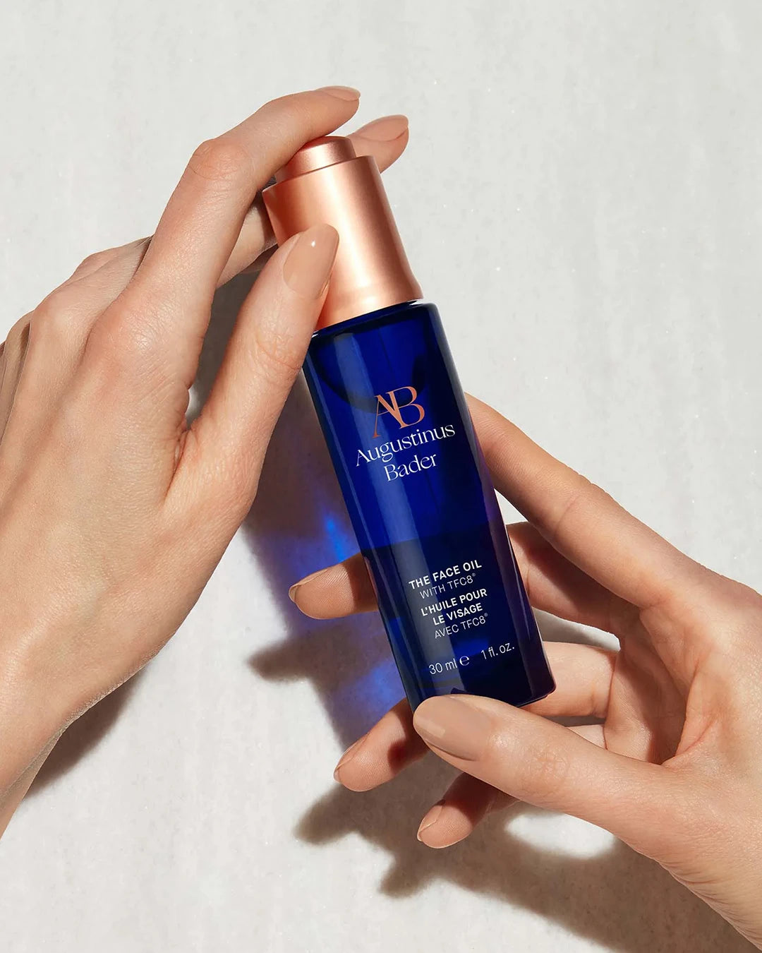 Hand holding a blue skincare bottle with a rose gold cap on a light background