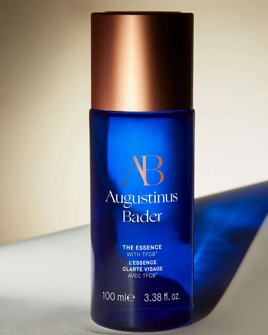 Blue skincare bottle with bronze cap labeled 'Augustinus Bader' on a neutral background