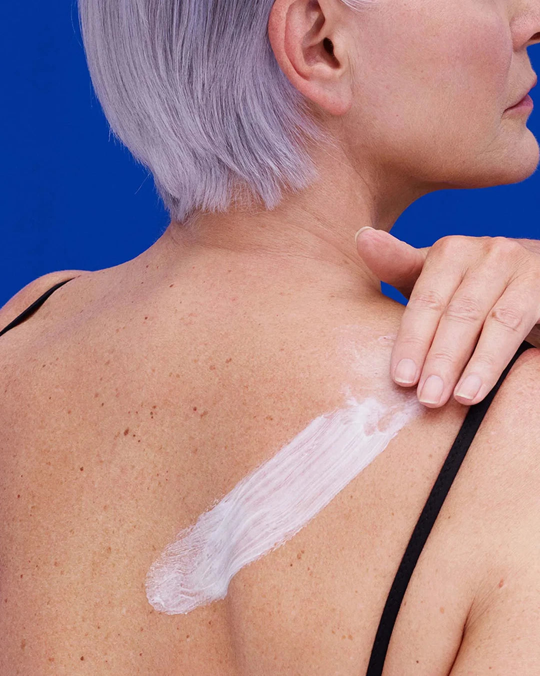 Person applying sunscreen to their shoulder with a blue background