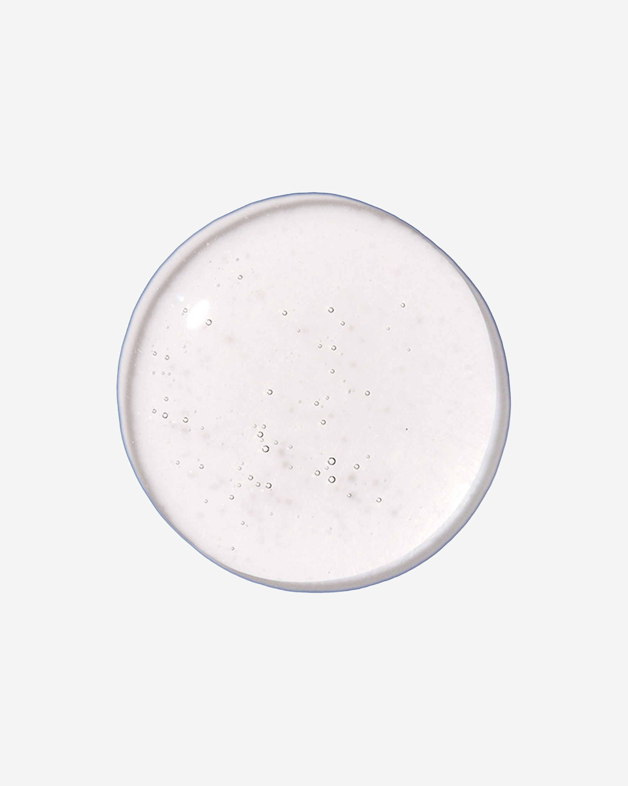 A top-down close-up view of a perfectly round, clear liquid droplet containing tiny air bubbles against a light gray background.