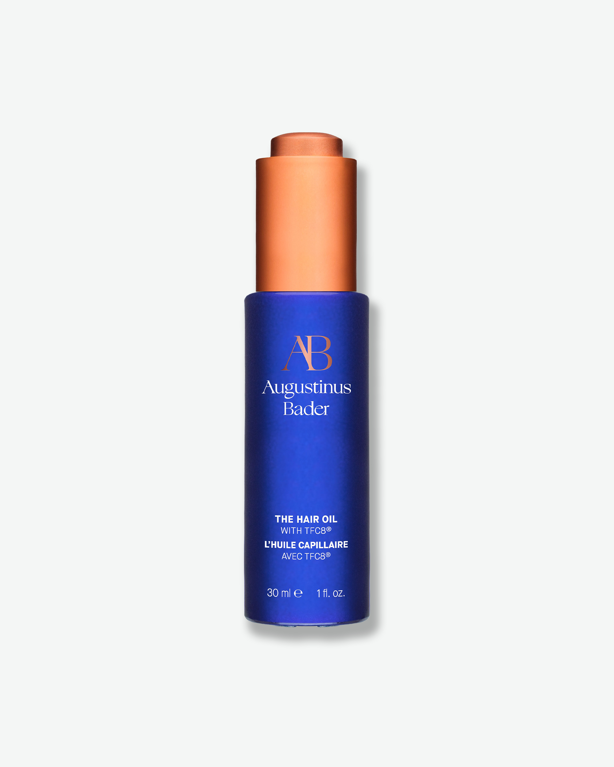 Blue bottle with copper cap of Augustinus Bader hair oil on a white background
